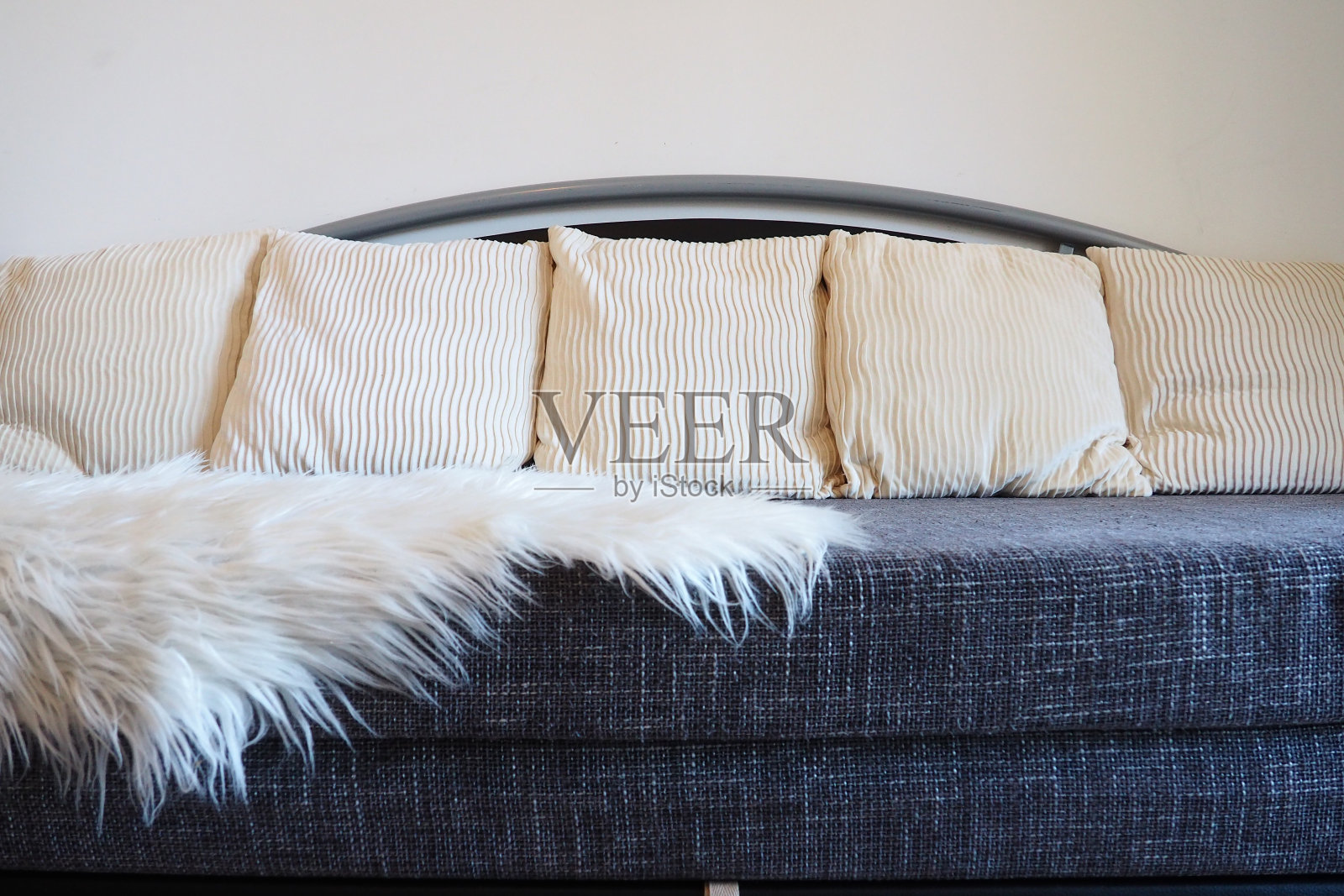 灰色沙发，粗糙的软垫织物和白色装饰凹槽靠垫。座位上盖着一长堆白色人造毛皮地毯或被单。客厅内饰照片摄影图片