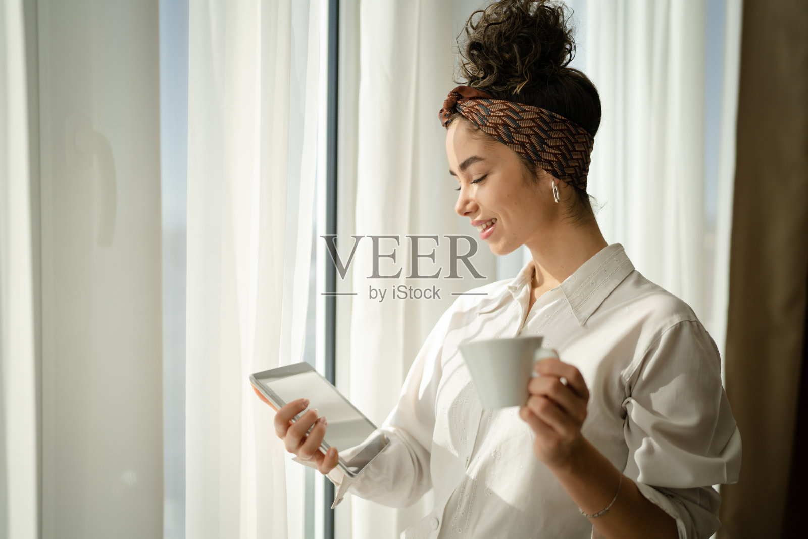 女人拿着平板电脑和一杯咖啡站在窗口工作照片摄影图片
