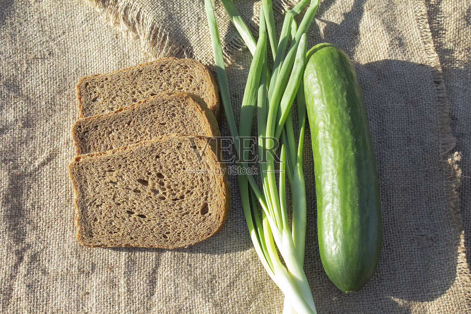 傍晚日落时分，野餐桌上放着黑面包、黄瓜和洋葱毛。照片摄影图片