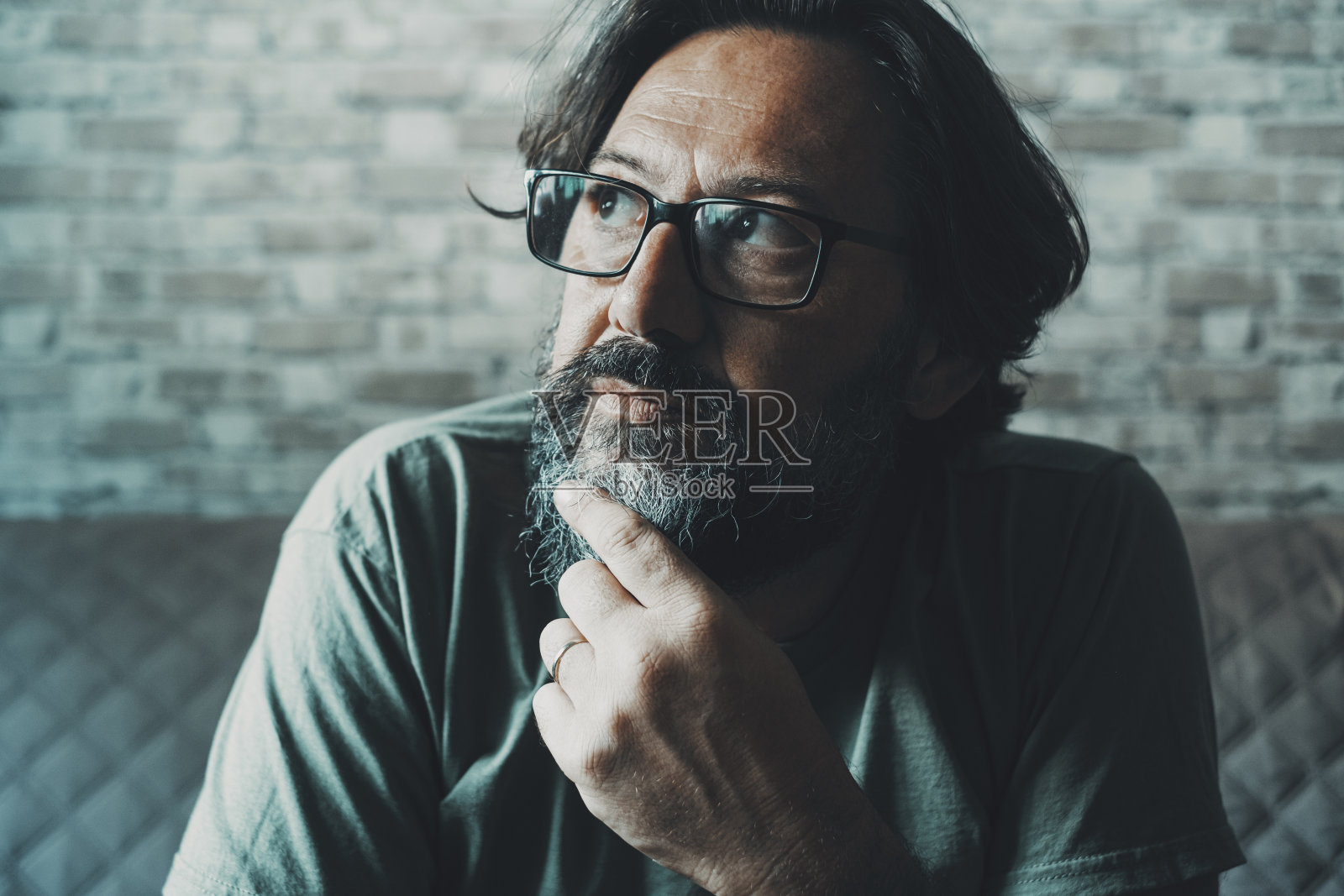 近距离的肖像，体贴的男人触摸他的下巴，在家里的沙发上看着眼镜。成年孤独男子思考解决方案。成熟的人有家庭经济困难的思想照片摄影图片