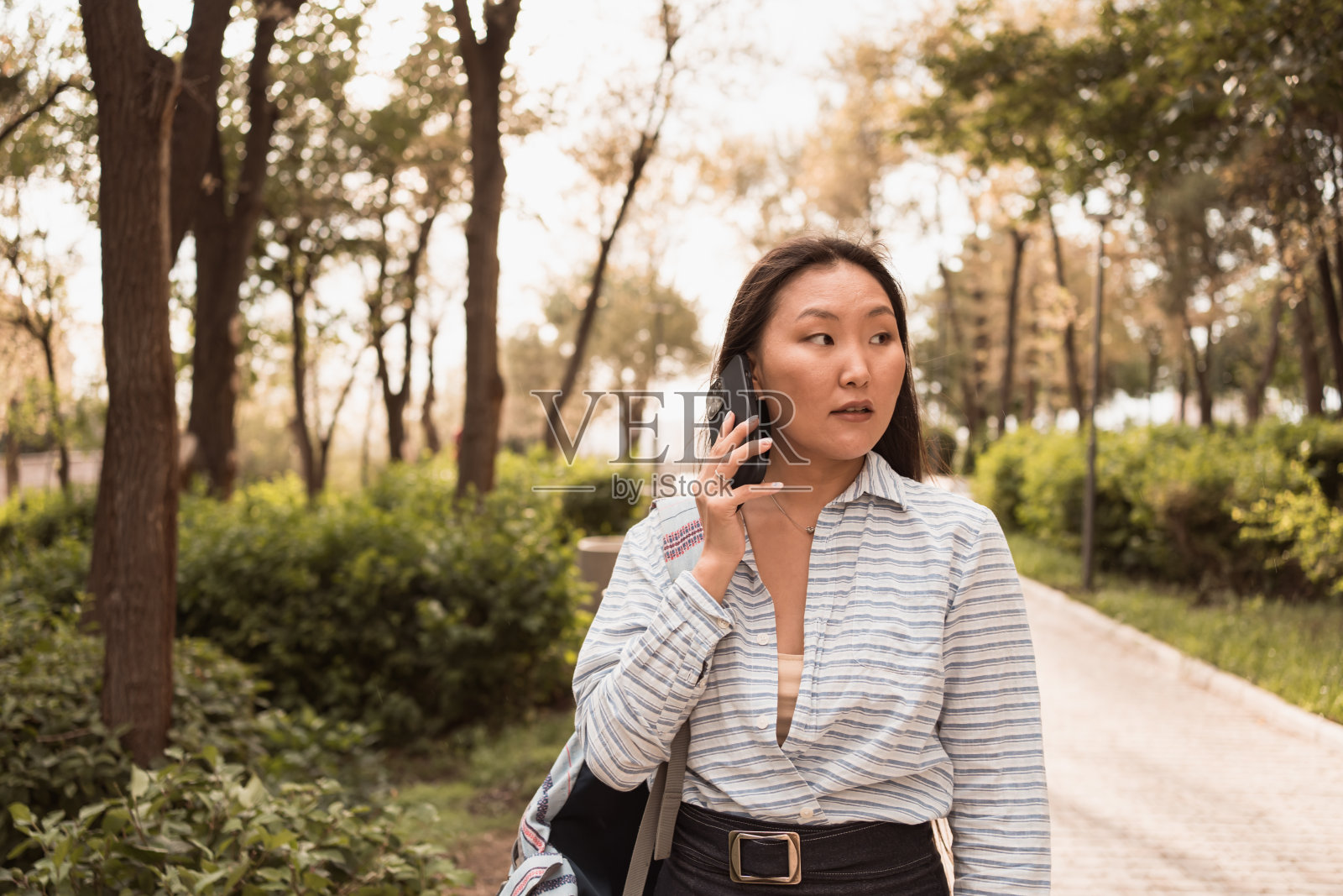 年轻的亚洲女子在夏日阳光明媚的一天在城市公园打电话照片摄影图片