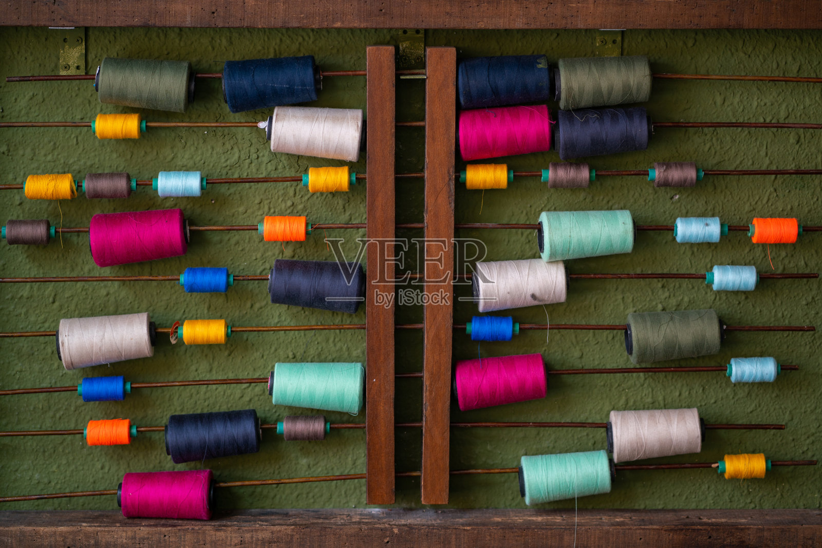 色彩鲜艳的缝纫线挂在旧木棍上，靠着绿色的纹理墙。照片摄影图片