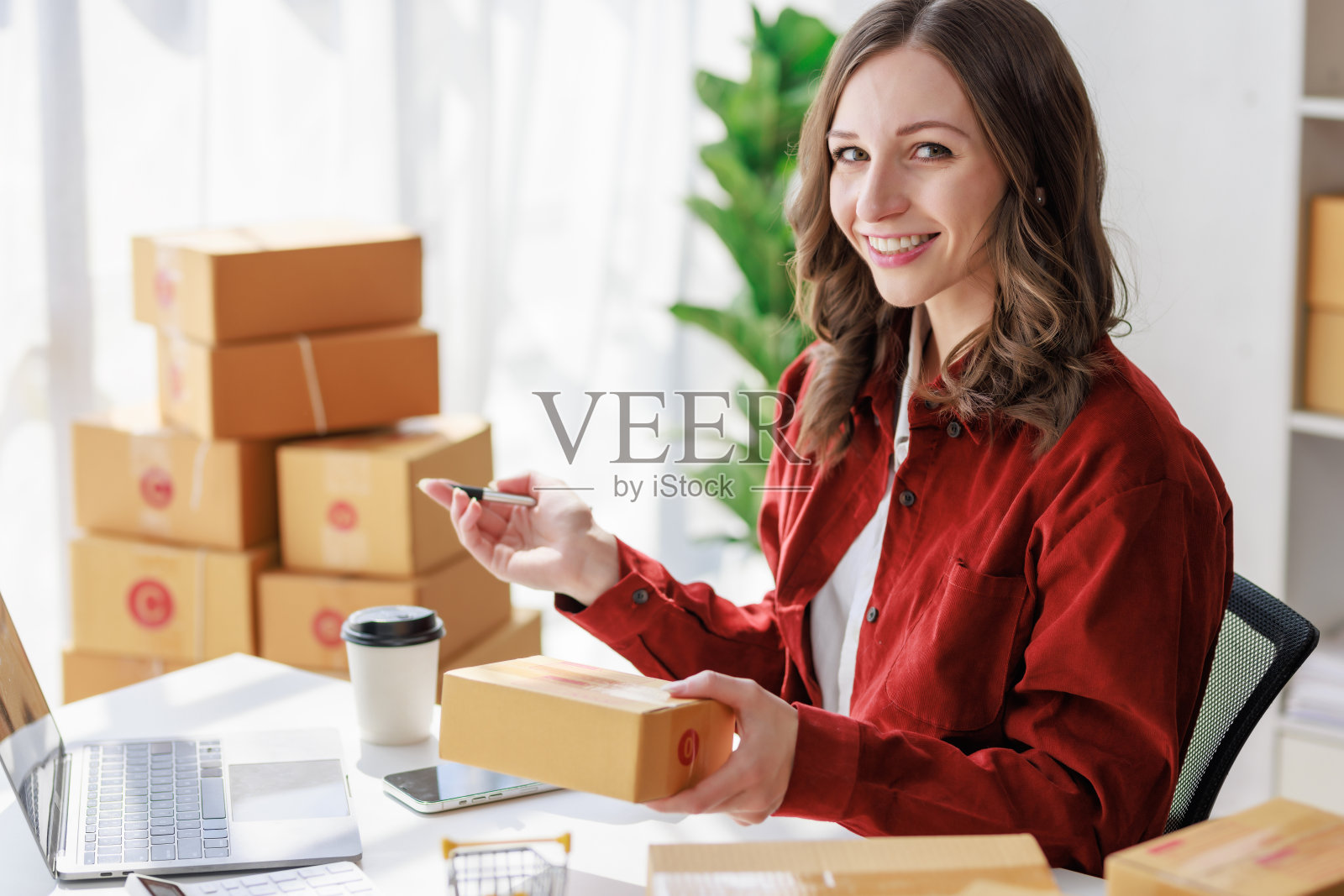 包裹递送和网上销售的概念，女性卖家或零售商在包裹盒子上写下客户的地址，准备送货，并使用笔记本电脑在网上商店检查当天的销售情况照片摄影图片