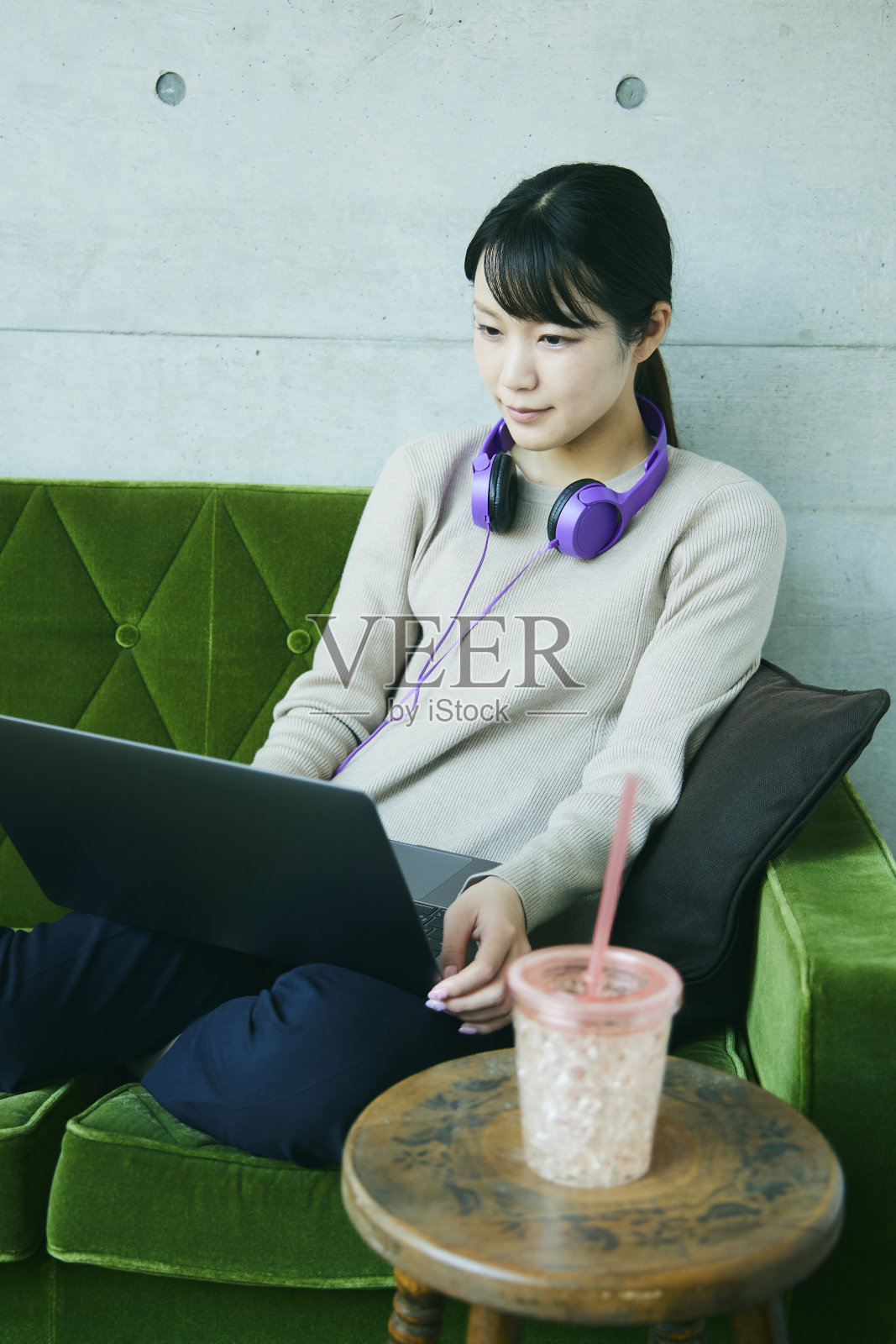 一位女士在绿色沙发上休息。她正在操作一台笔记本电脑。照片摄影图片