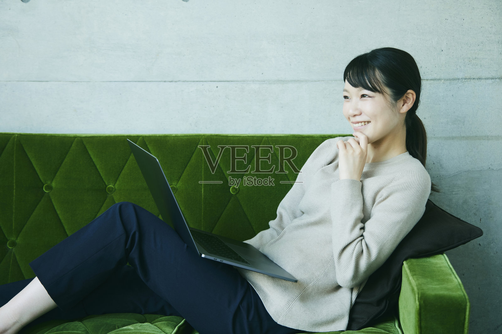 一位女士在绿色沙发上休息。她正在操作一台笔记本电脑。照片摄影图片