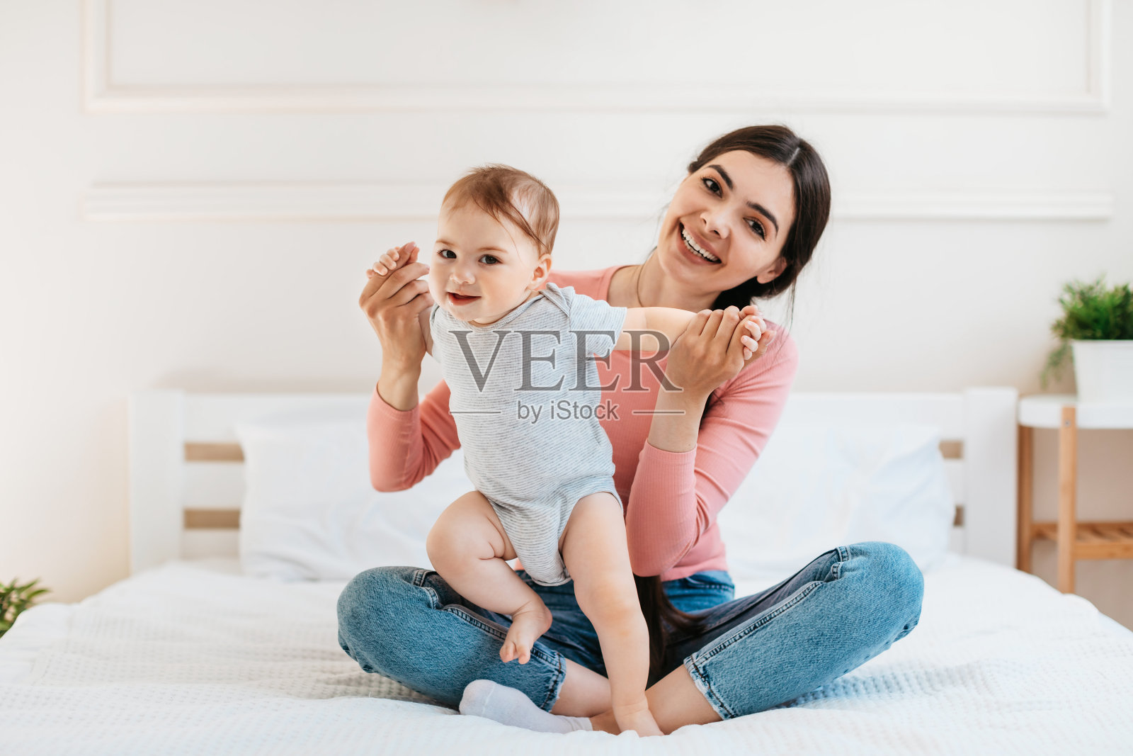 快乐的年轻妈妈帮助她的婴儿迈出第一步，坐在床上，与孩子共度时光照片摄影图片