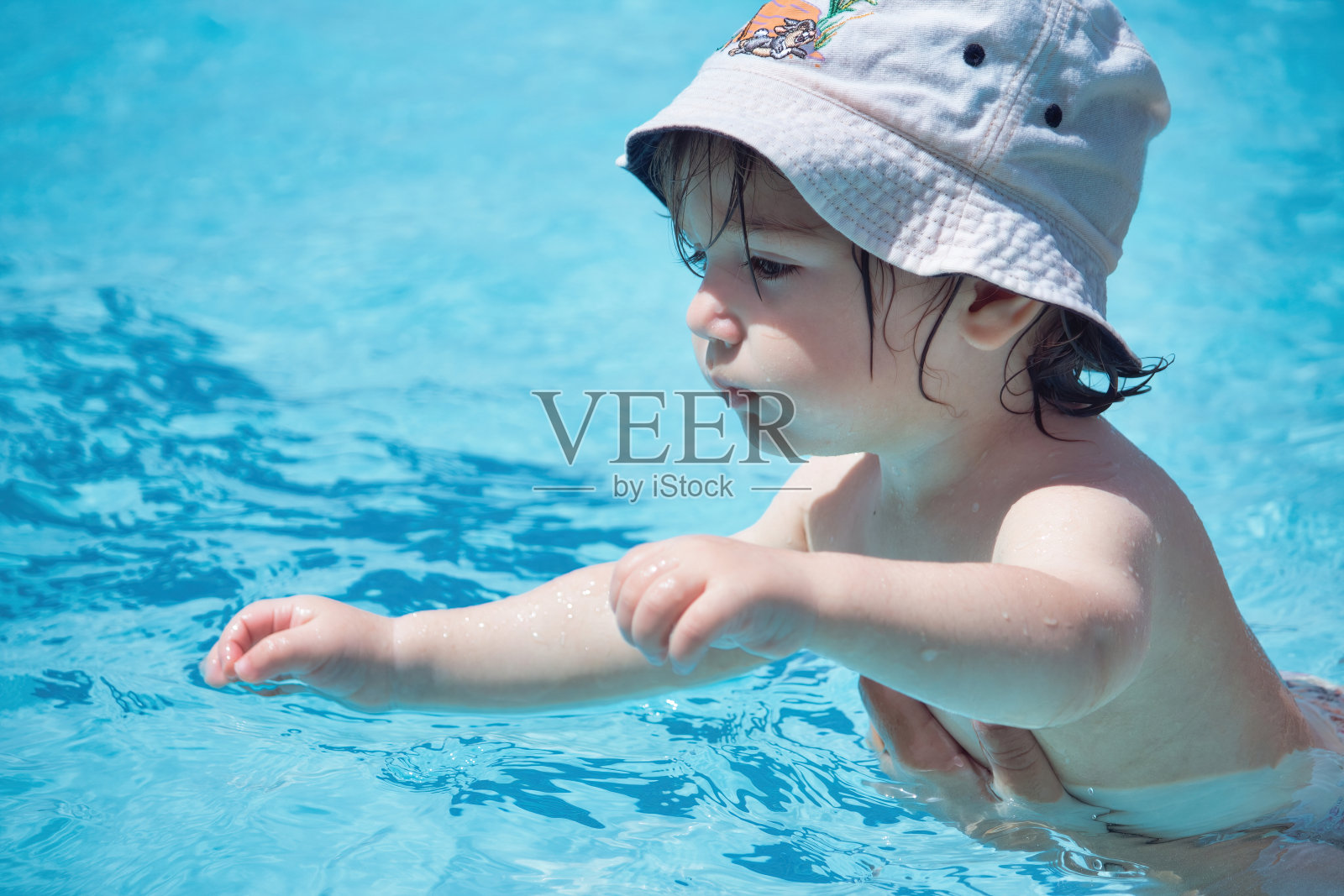 一个年轻的白人男孩戴着帽子在温泉池游泳，由他的父母支持照片摄影图片