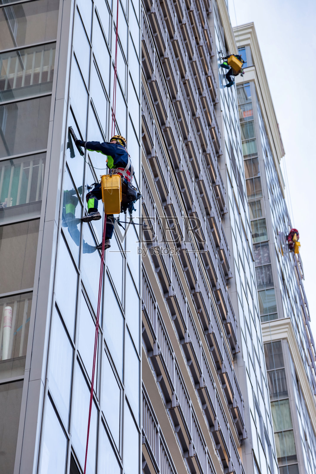 职业工业登山者工人清洗外立面玻璃，悬挂在建筑上，从下面看。绳索进入工人攀爬墙屋。城市风险作品概念。复制广告空间照片摄影图片