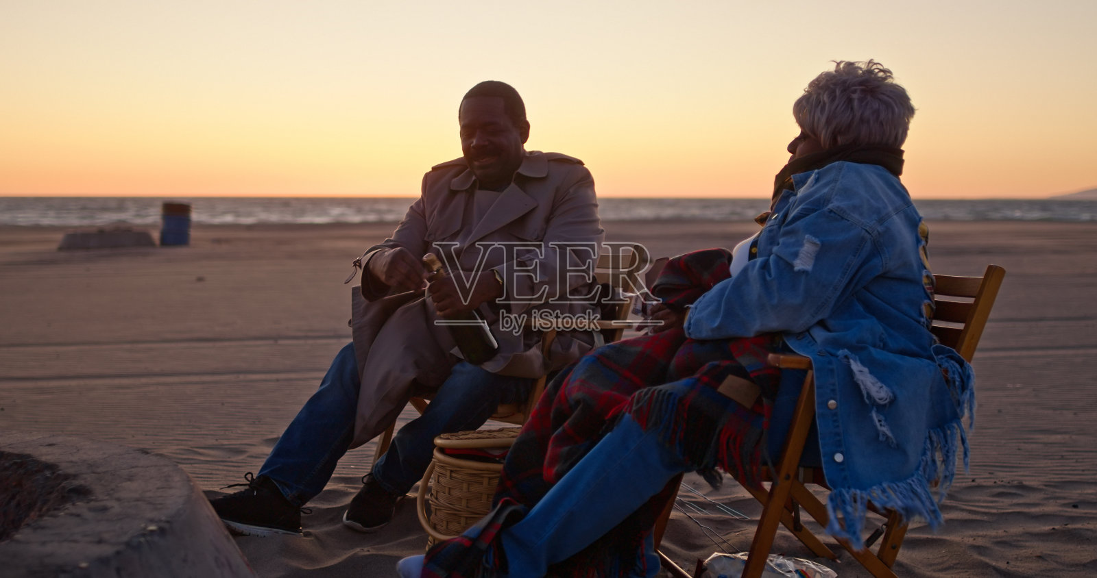 日落时分，坐在海滩上拿着棉花糖的非裔美国老夫妇照片摄影图片