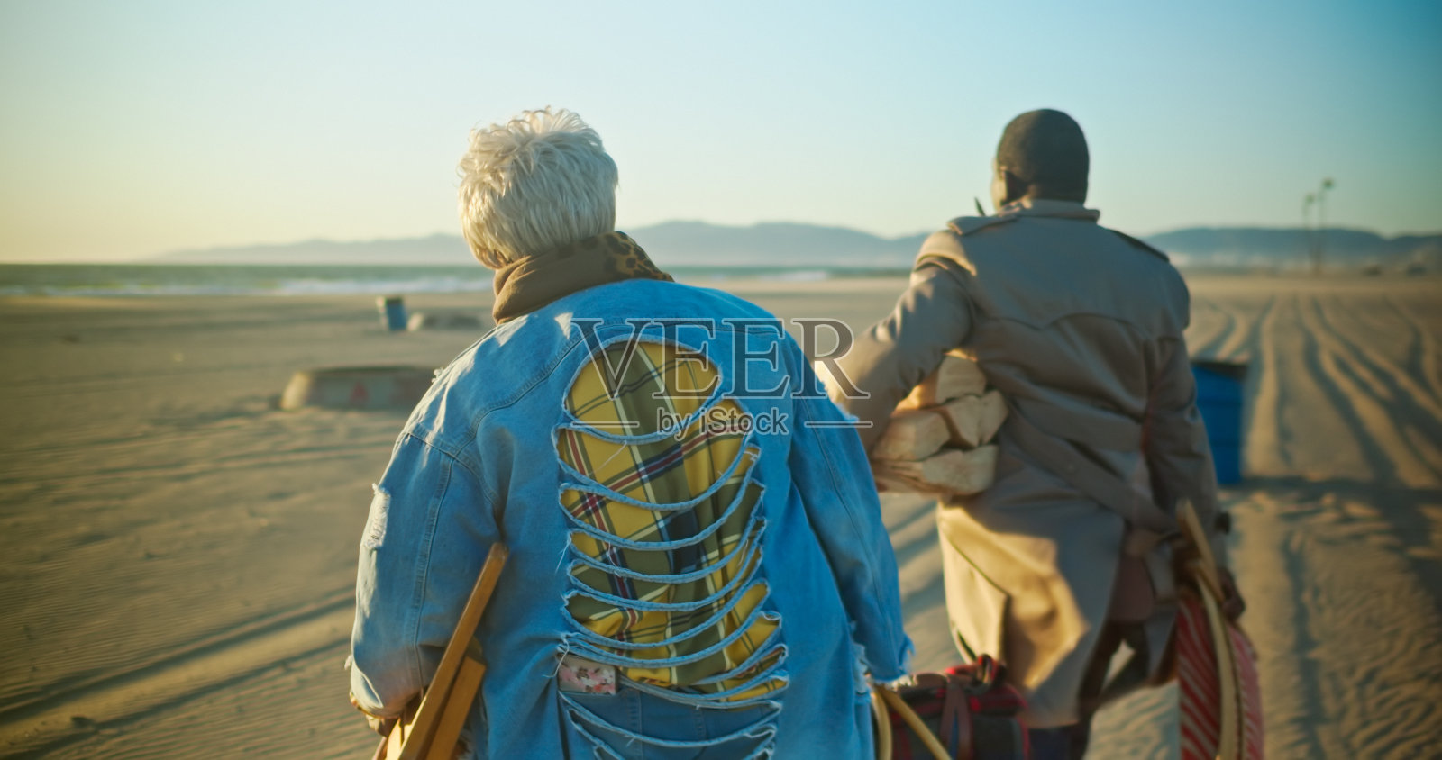 年长的非裔美国夫妇在日落时带着野餐用品穿过海滩照片摄影图片