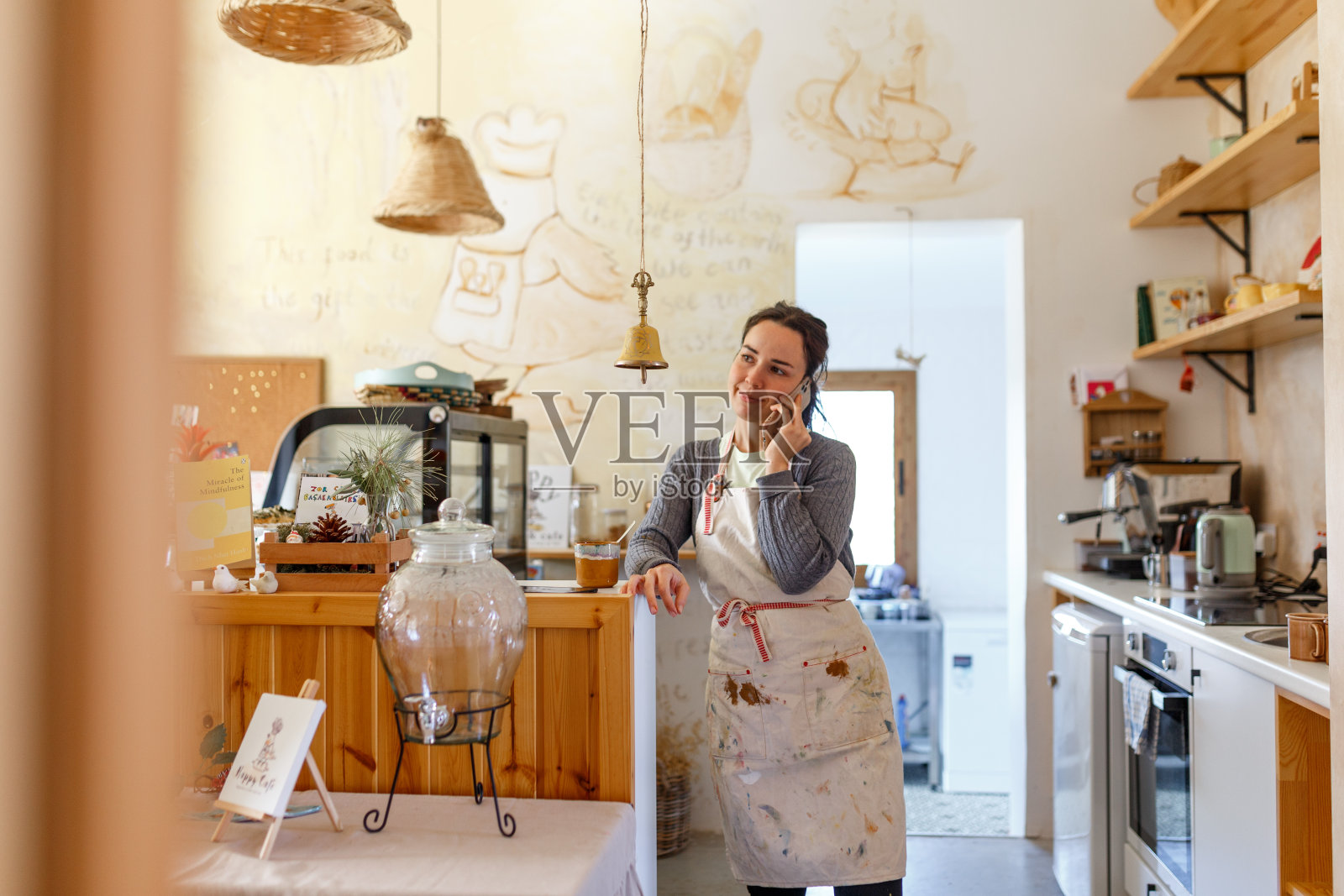 年轻的女咖啡师站在吧台后面，在咖啡馆里用智能手机聊天，小企业主的概念，真实的设计照片摄影图片