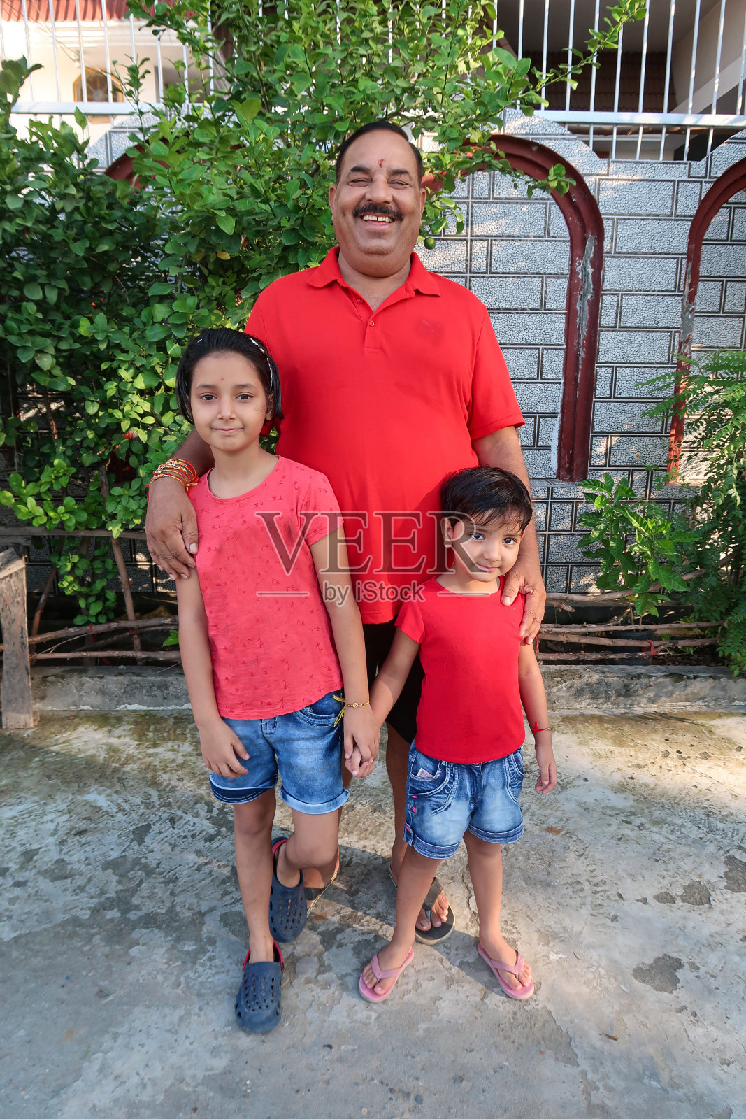 印度人的形象，印度家庭成员，祖父和孙子，男人和孩子穿着休闲的t恤和短裤，站在铺好的院子里，重点是前景照片摄影图片