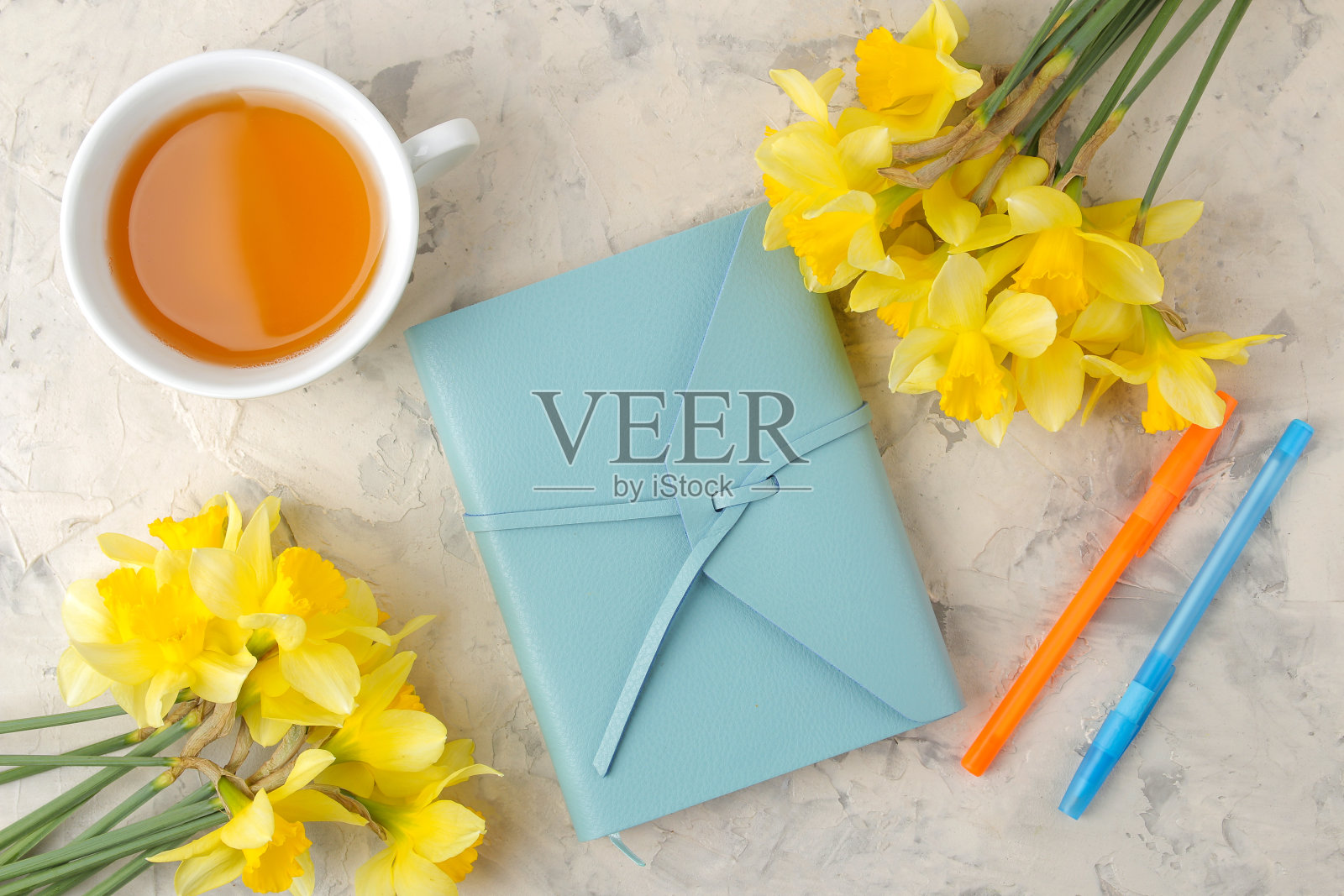春天的花朵，黄色的水仙花，一杯茶，一本笔记本放在浅色的混凝土背景上。俯视图照片摄影图片