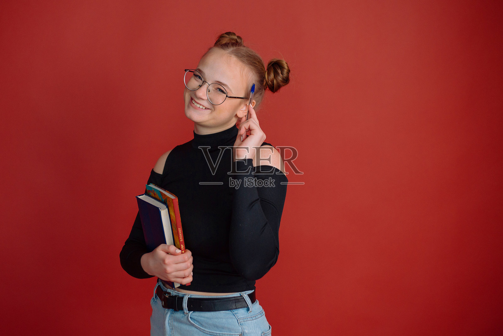 一名身穿黑色上衣、梳着发髻的年轻女子拿着笔记本和红底笔。大学的学生。大学教育。教育。学校。考试和分数。学生会话照片摄影图片