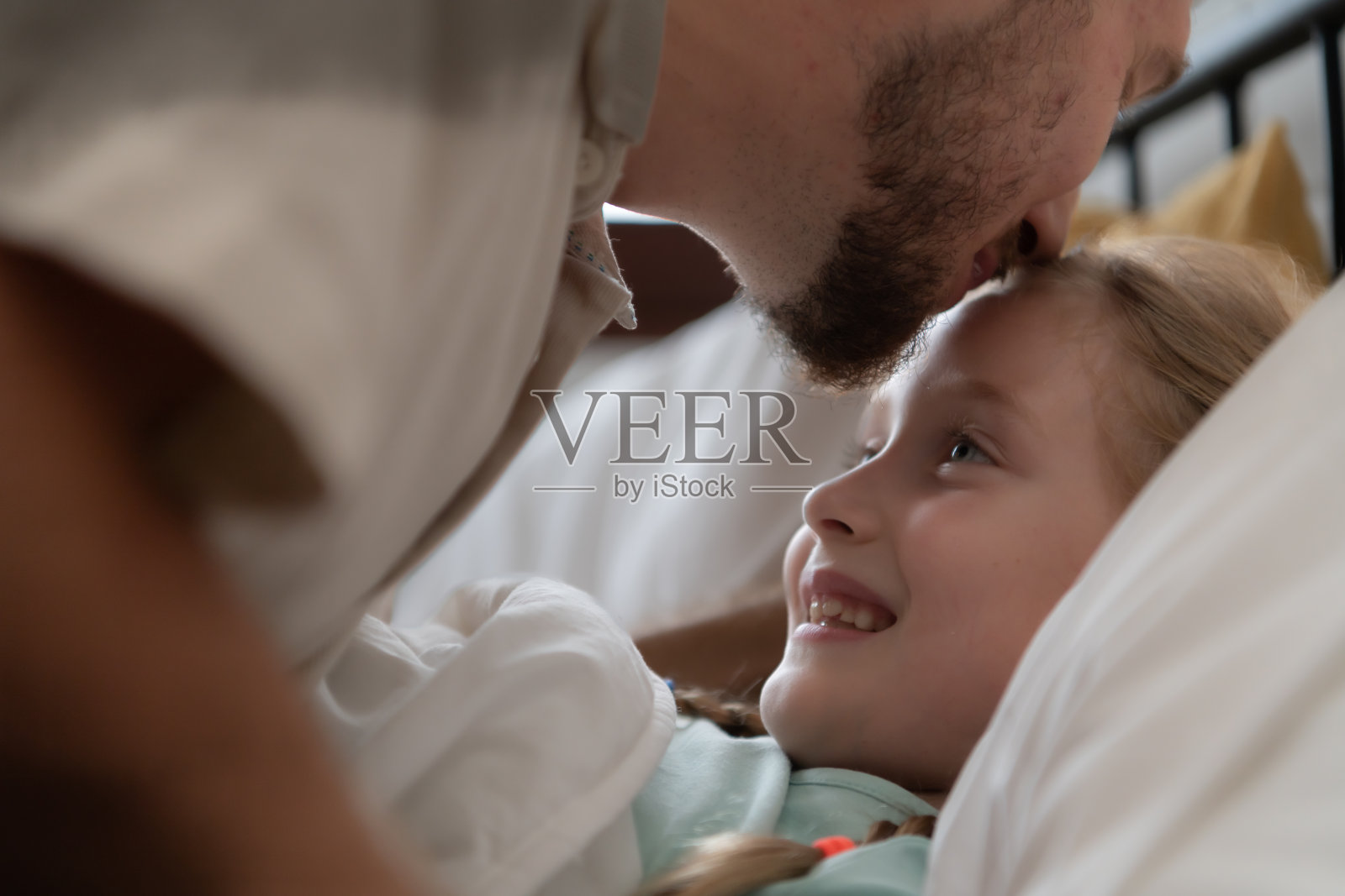 在晚上睡觉前，父亲会亲吻女儿的额头来表达自己的爱意。睡个好觉照片摄影图片