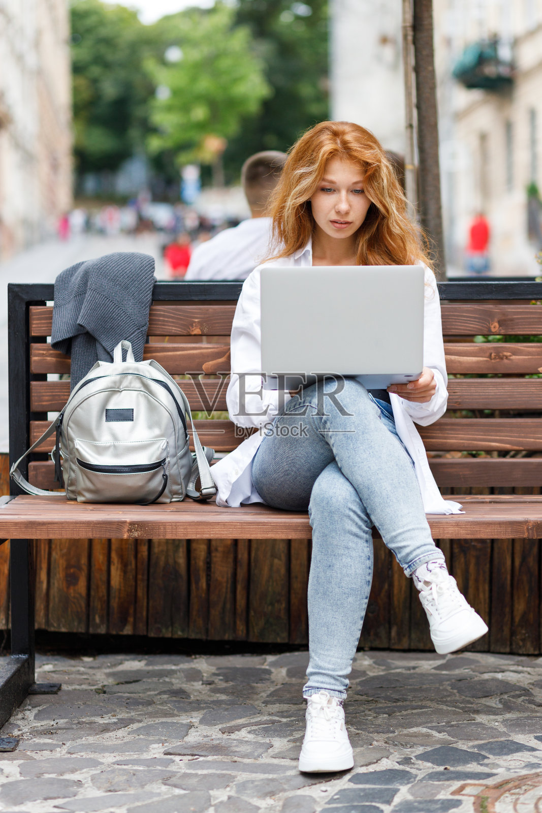 一名年轻女子坐在街边的长椅上，用笔记本电脑专心工作照片摄影图片