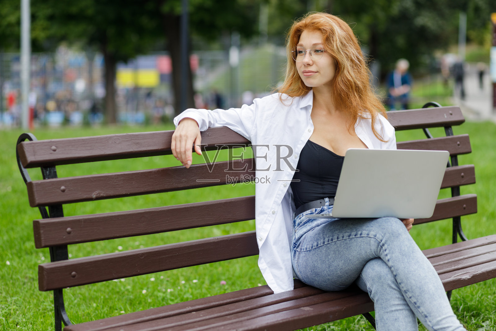 放松年轻的红发女子坐在公园和使用她的笔记本电脑照片摄影图片