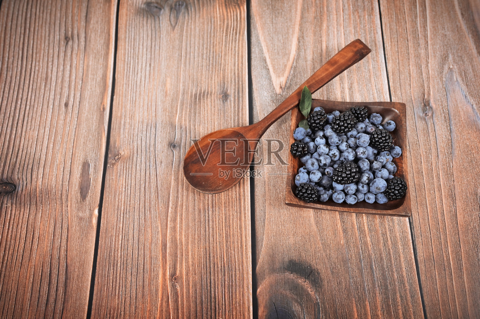 新鲜采摘的多汁的蓝莓和黑莓放在一个木碗里，放在一张质朴的桌子上。木制背景上的蓝莓。蓝莓中的抗氧化剂。健康饮食的概念照片摄影图片