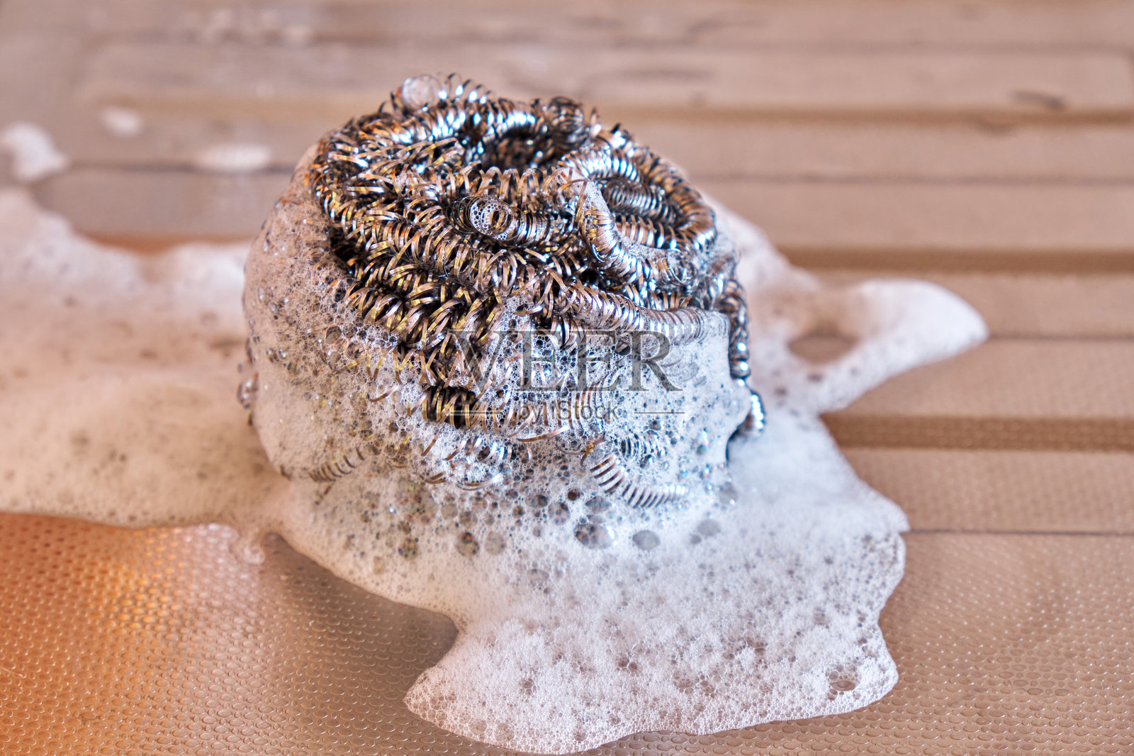 厨房里的金属螺旋海绵浸在洗涤泡沫中，放在不锈钢水槽上。近距离照片摄影图片