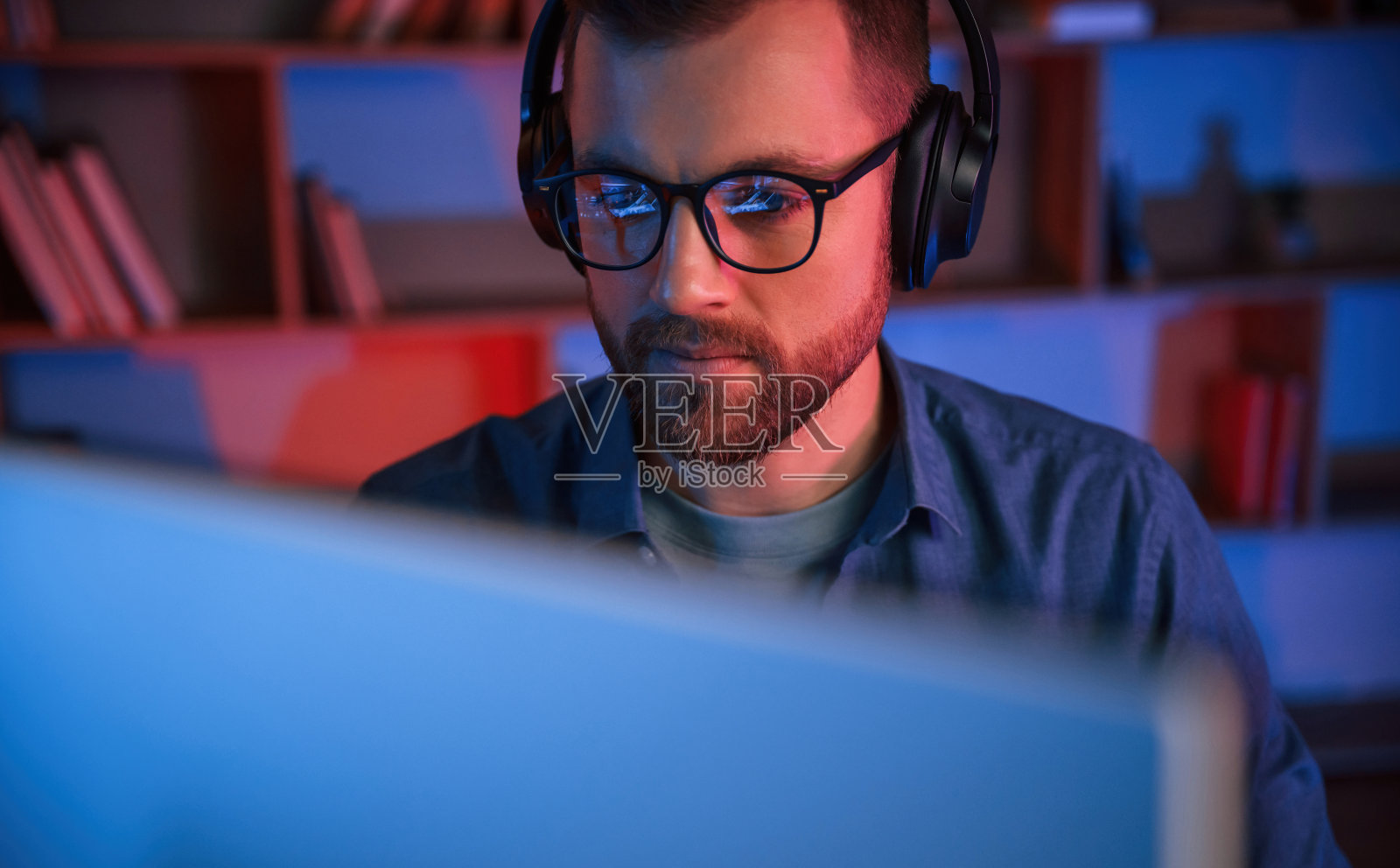 前视图。一名男子坐在家里的电脑前。霓虹灯照明照片摄影图片