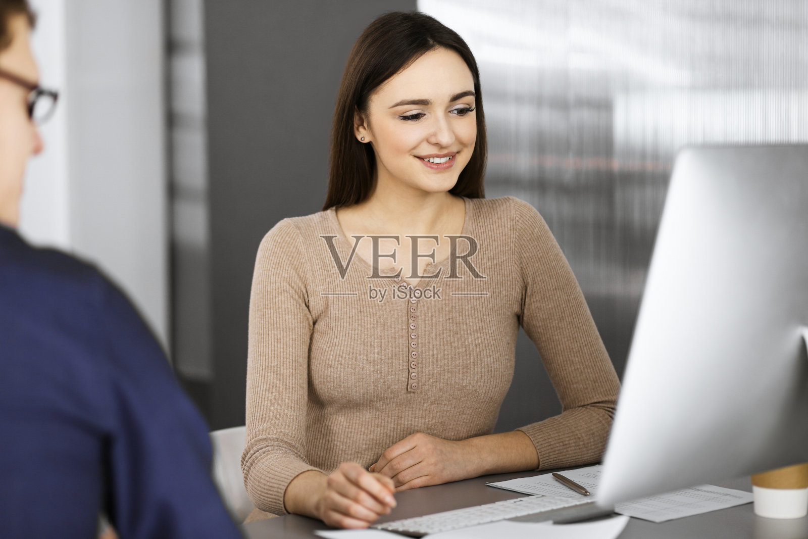 在现代办公室里，年轻的商务人士坐在办公桌前互相交谈。商业成功的概念照片摄影图片