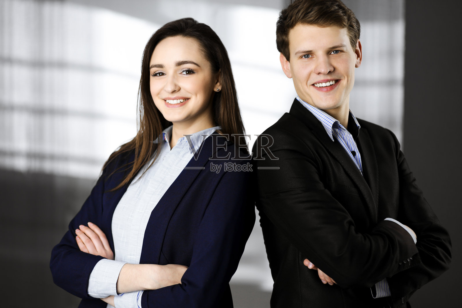 友好的年轻同事们抱臂站在一个现代化的办公室里。工作中的成功商业人士的肖像照片摄影图片