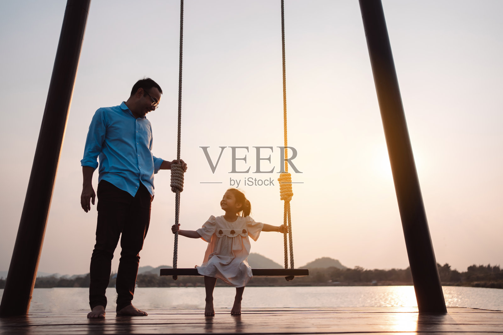 快乐的家庭在公园里荡秋千，在大自然中享受日落，周末的家庭生活活动。照片摄影图片