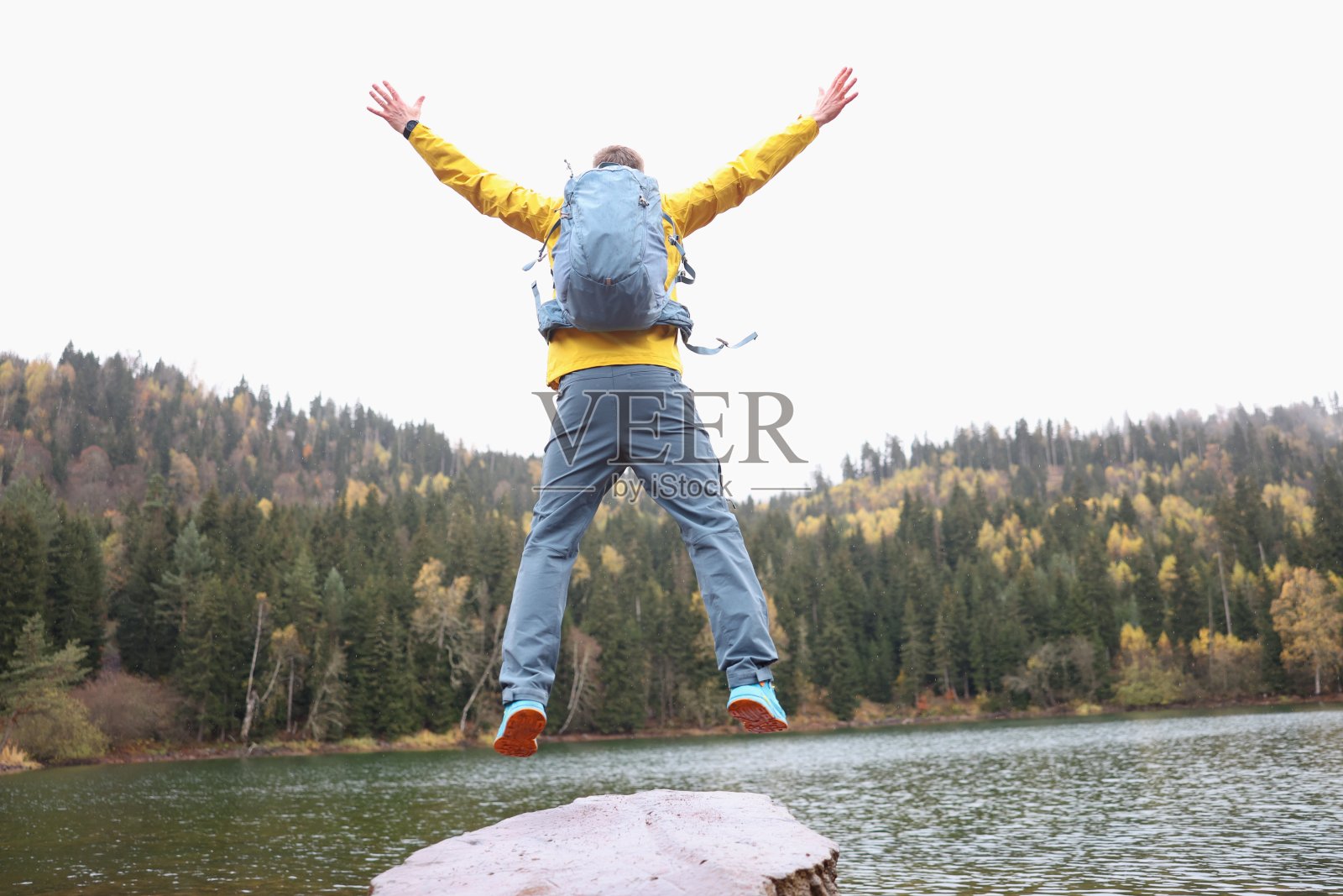快乐的男性旅行者与背包跳在森林湖附近，而达到目标的背影特写照片摄影图片