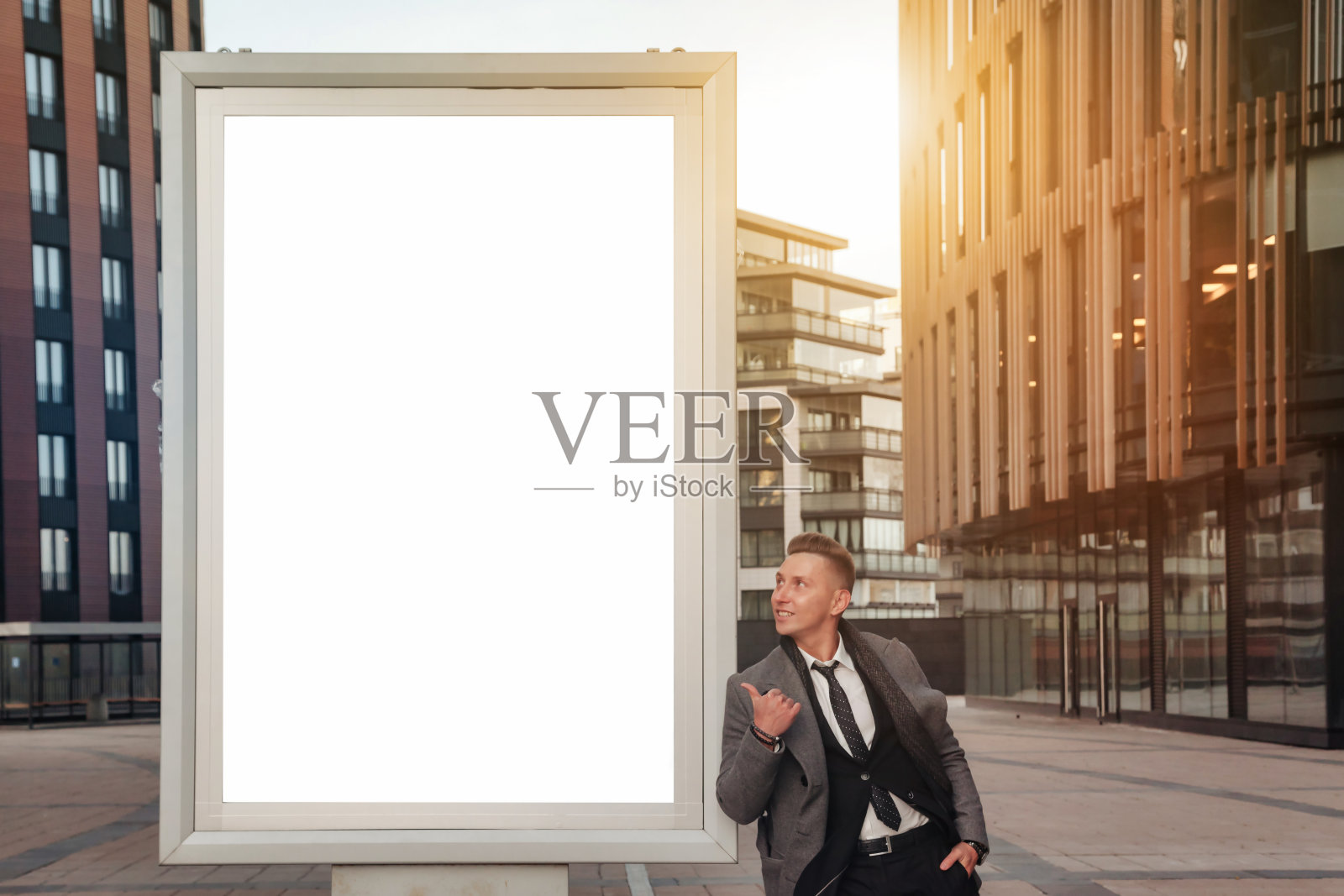 西装革履的自信青年商人指着商业大厦旁的空横幅，看着广告牌。这家伙在金融区的办公楼附近拍照。复制广告文字空间照片摄影图片