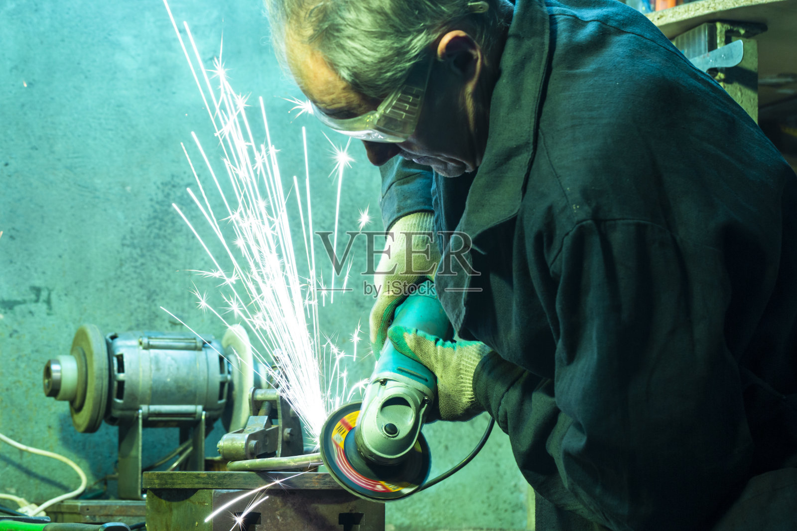 男钳工戴着防护手套和制服，在车间里用磨刀工具进行金属加工。照片摄影图片