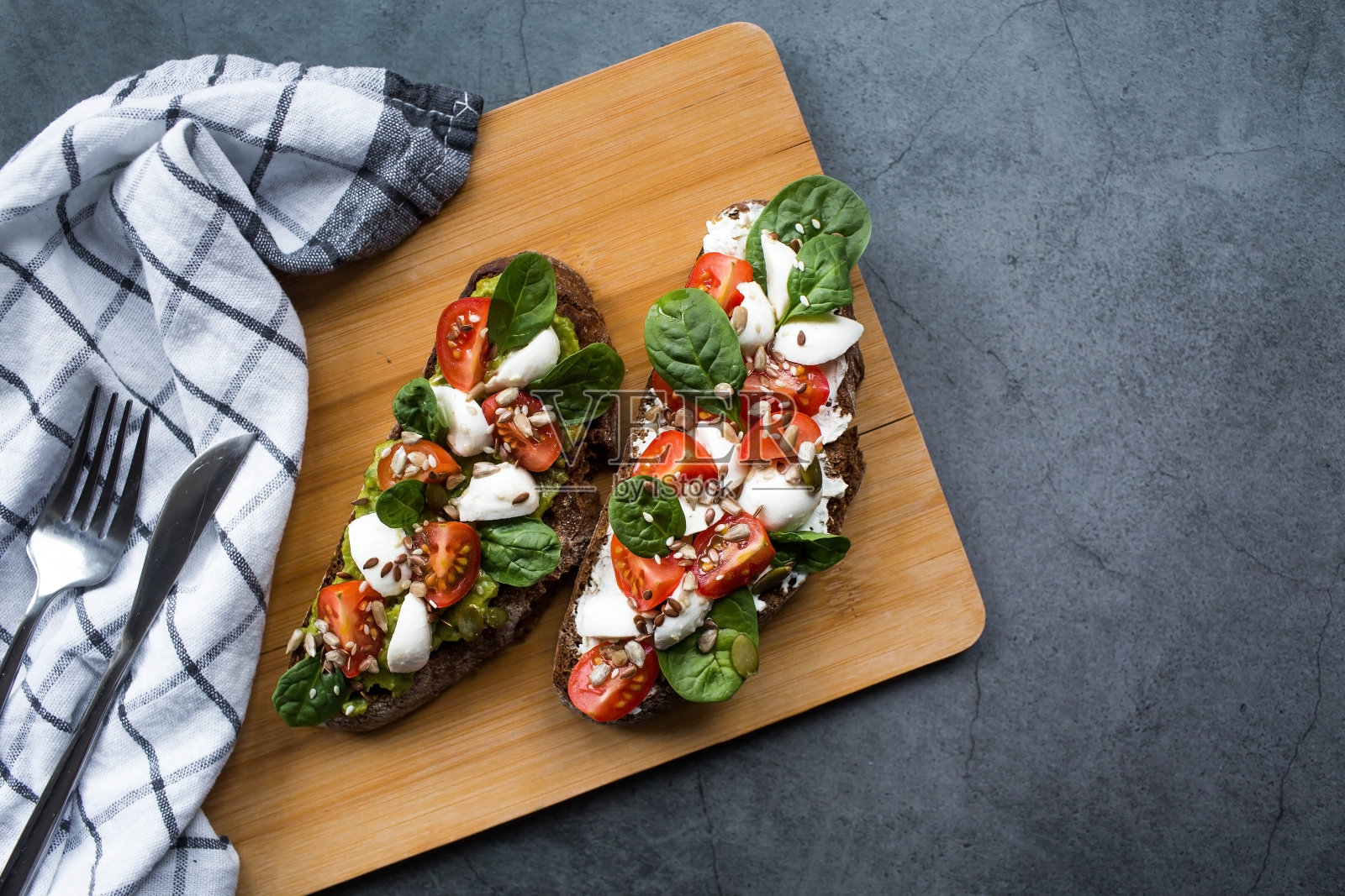 意式烤面包(三明治)，配圣女果、马苏里拉奶酪和香草，放在砧板上，背景为黑色。传统的意大利小吃。照片摄影图片