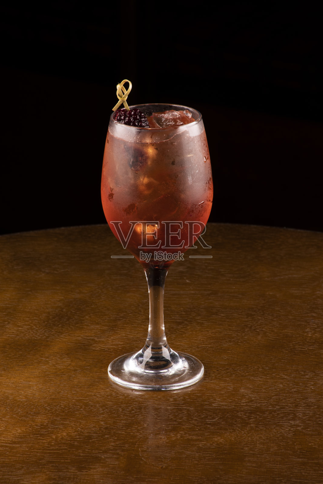 一杯鸡尾酒，以玫瑰玫瑰葡萄酒和浆果为装饰，并将冰块隔离在木桌和黑色背景上照片摄影图片