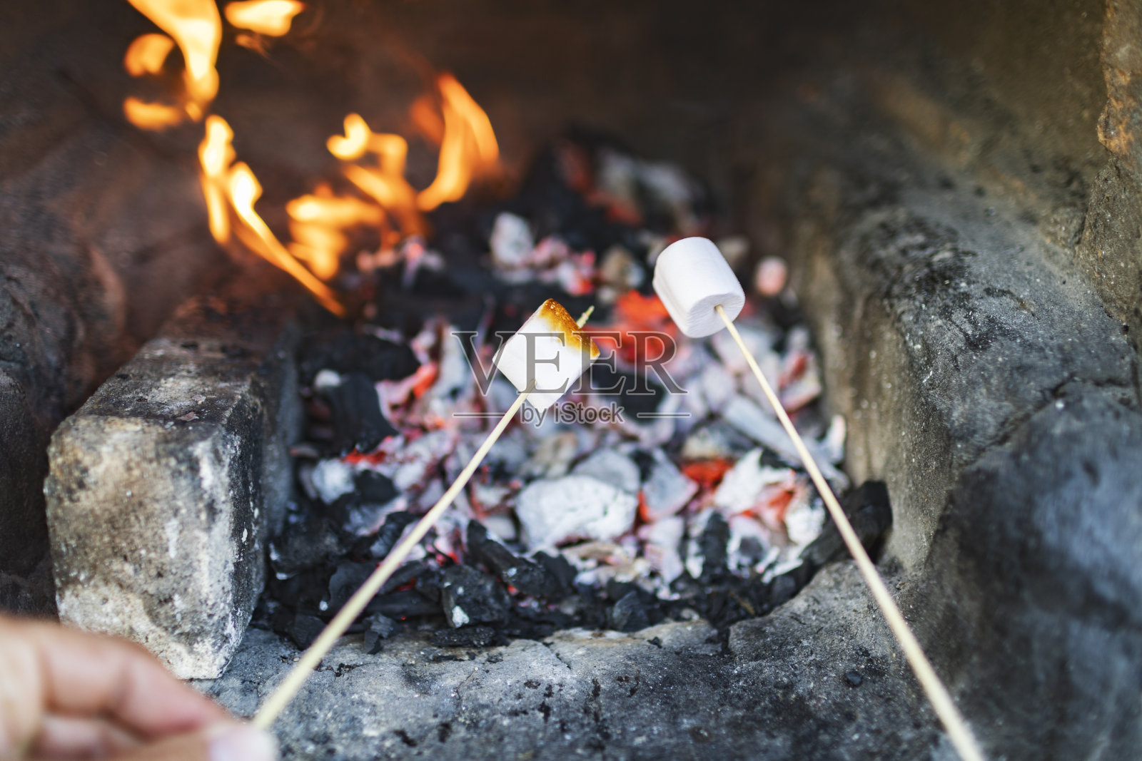 近距离的手拿棉花糖棒在火照片摄影图片