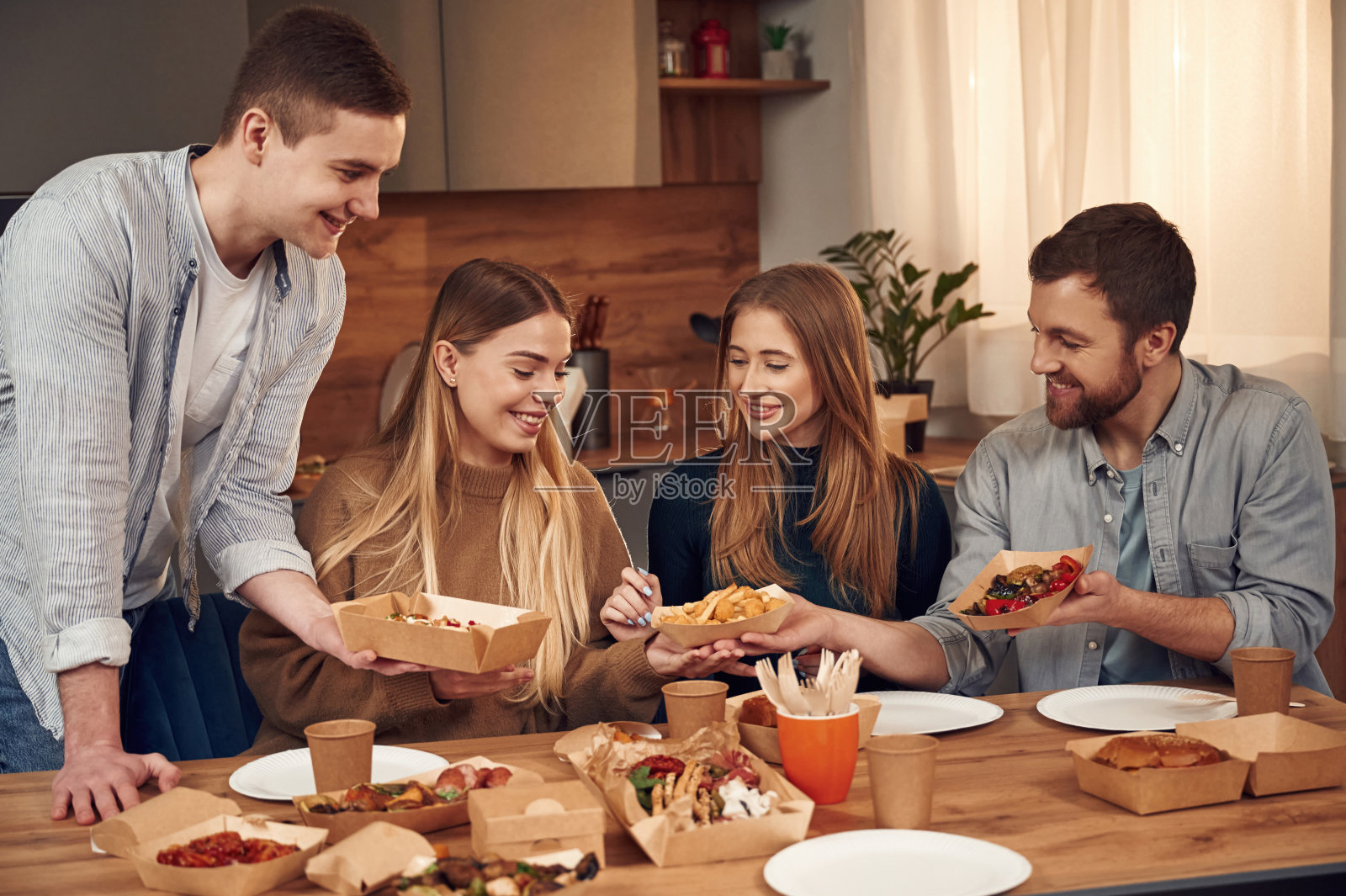 在桌子旁边。朋友们坐在家里一起吃饭照片摄影图片