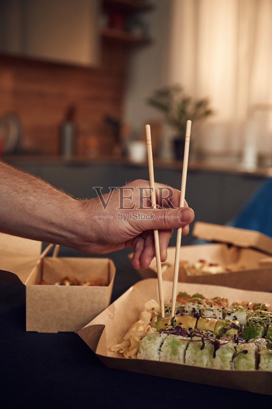 使用筷子。一个穿着便服的男人拿着装在环保纸盒里的寿司照片摄影图片