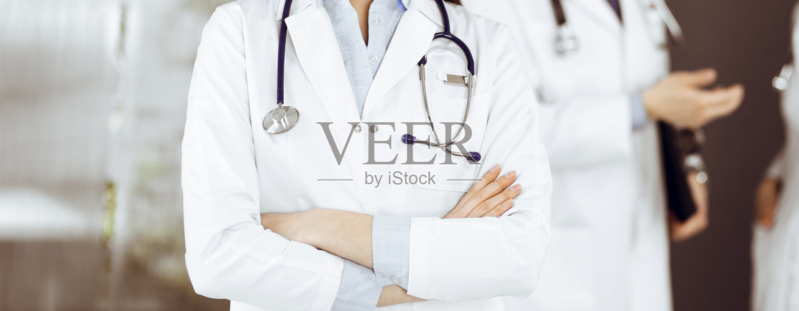 无名年轻女医生双臂交叉站在诊所里。冠状病毒大流行期间的医学概念照片摄影图片