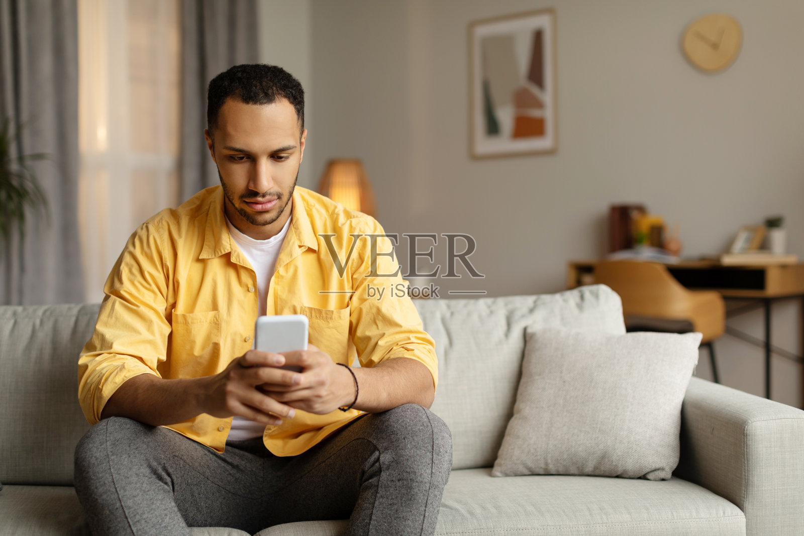 严肃的年轻黑人使用智能手机应用程序，坐在家里的沙发上，空白。小工具生活方式，移动应用程序照片摄影图片