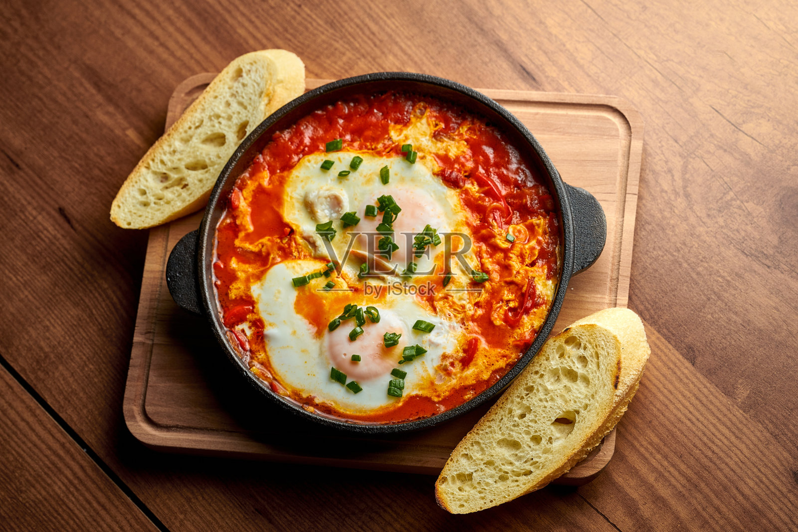 在平底锅里用西红柿、洋葱和皮塔饼煎鸡蛋，背景是木制的。美味Shakshuka照片摄影图片