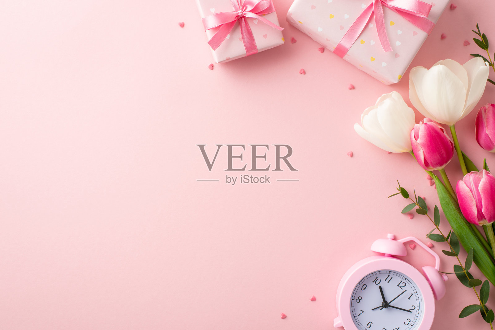 母亲节的概念。顶部视图照片礼盒彩带蝴蝶结花束的粉红色和白色郁金香闹钟和心形洒在孤立的粉彩粉红色背景与复制空间照片摄影图片