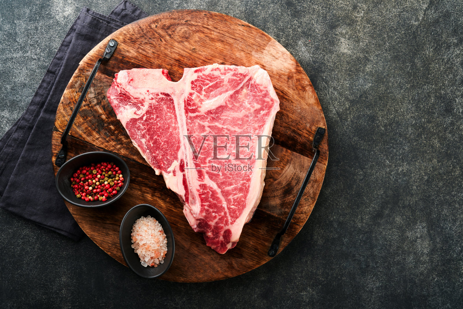 厚的生t骨牛排。干陈生丁字骨或上等腰牛肉用切好的猪排配上香草和盐，深色背景。俯视图和复制空间。照片摄影图片
