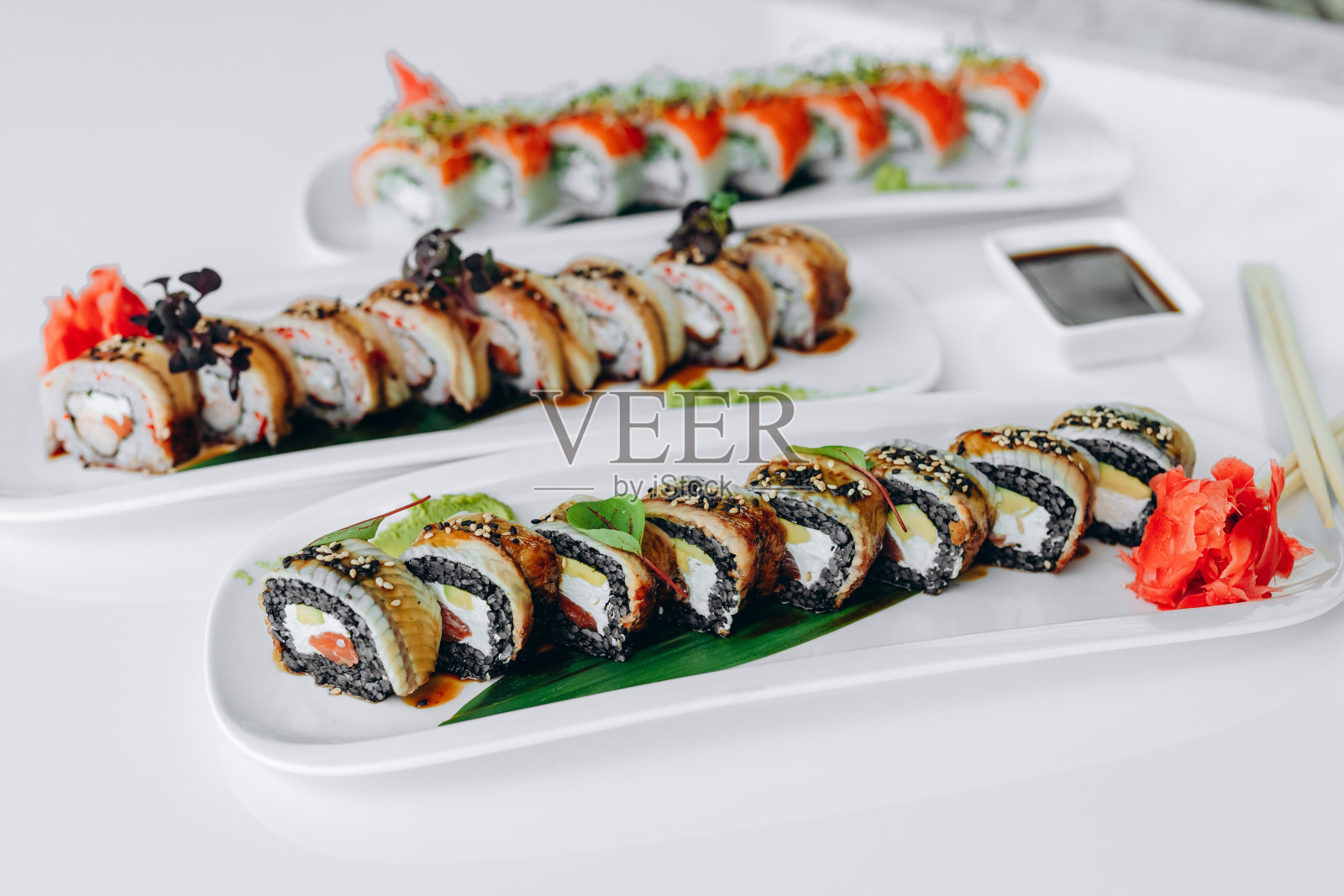 寿司，黑米、红鱼和黄瓜，放在白色的盘子里，点缀着绿色蔬菜。照片摄影图片