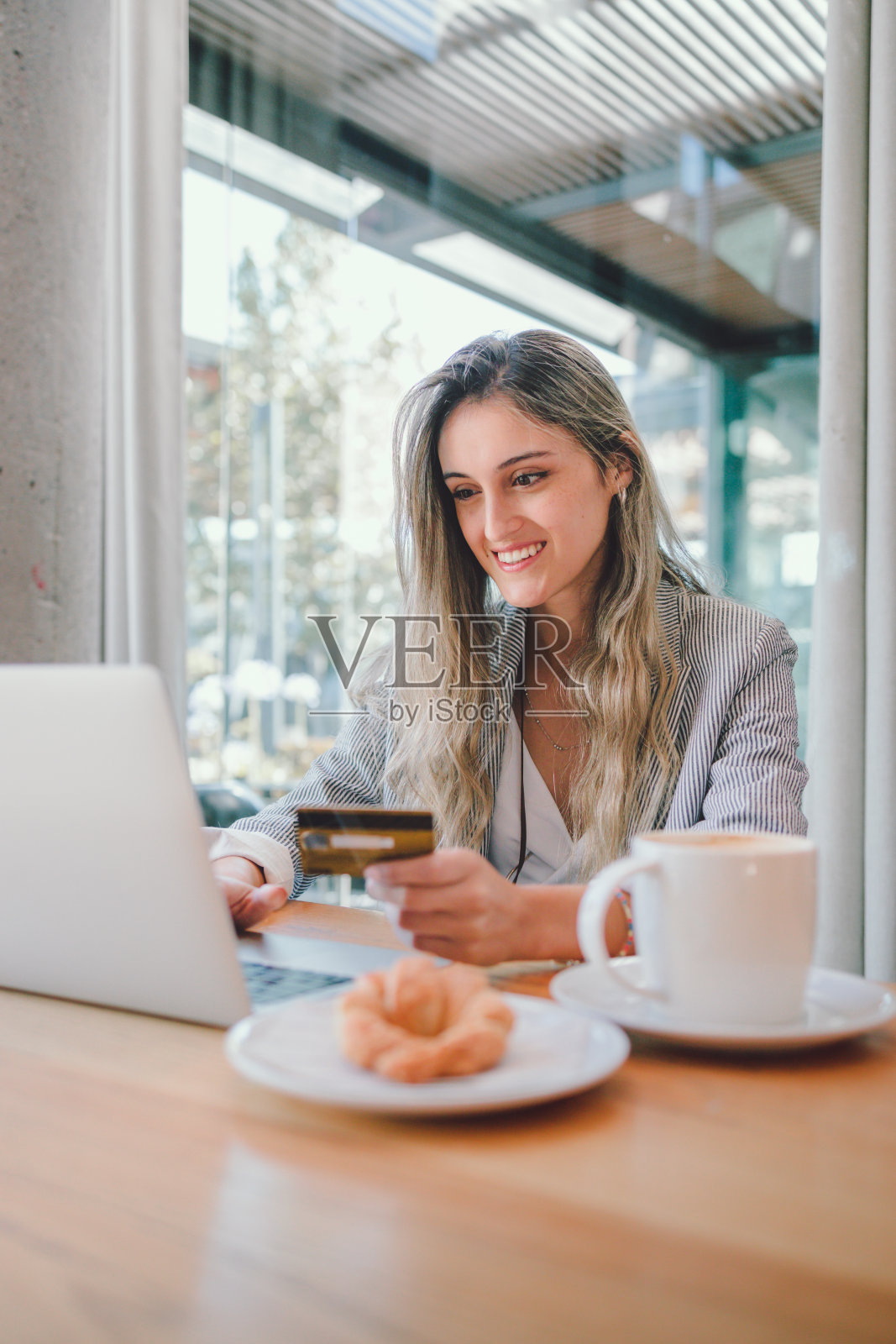 安静的千禧一代商业女性，使用信用卡和笔记本电脑，在现代工作场所喝一杯咖啡。照片摄影图片