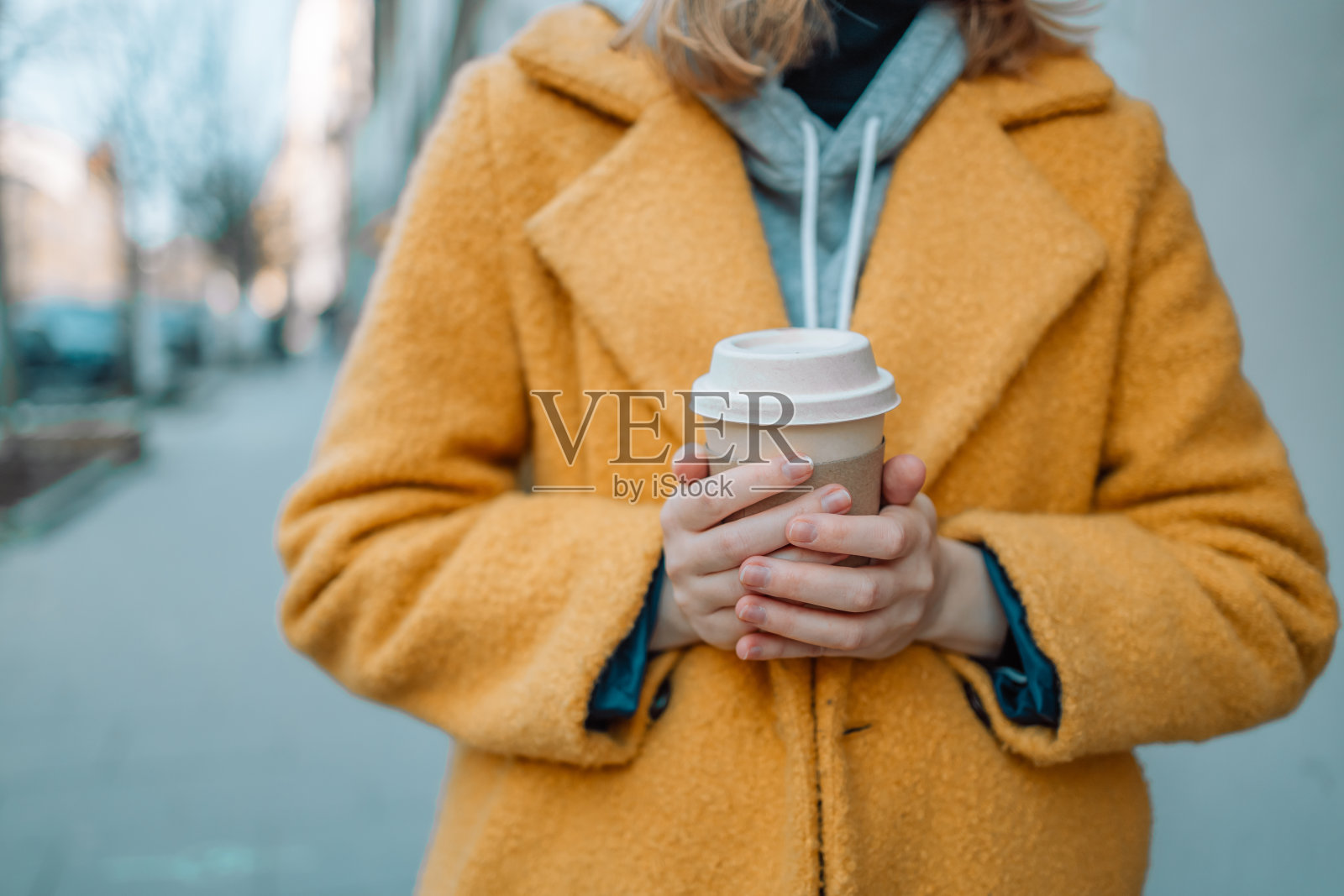 时尚快乐的年轻女子穿着亮黄色外套拿着咖啡走。戴着眼镜的微笑女孩的肖像，在欧洲老城区享受一杯茶，咖啡的自由时间旅行。照片摄影图片