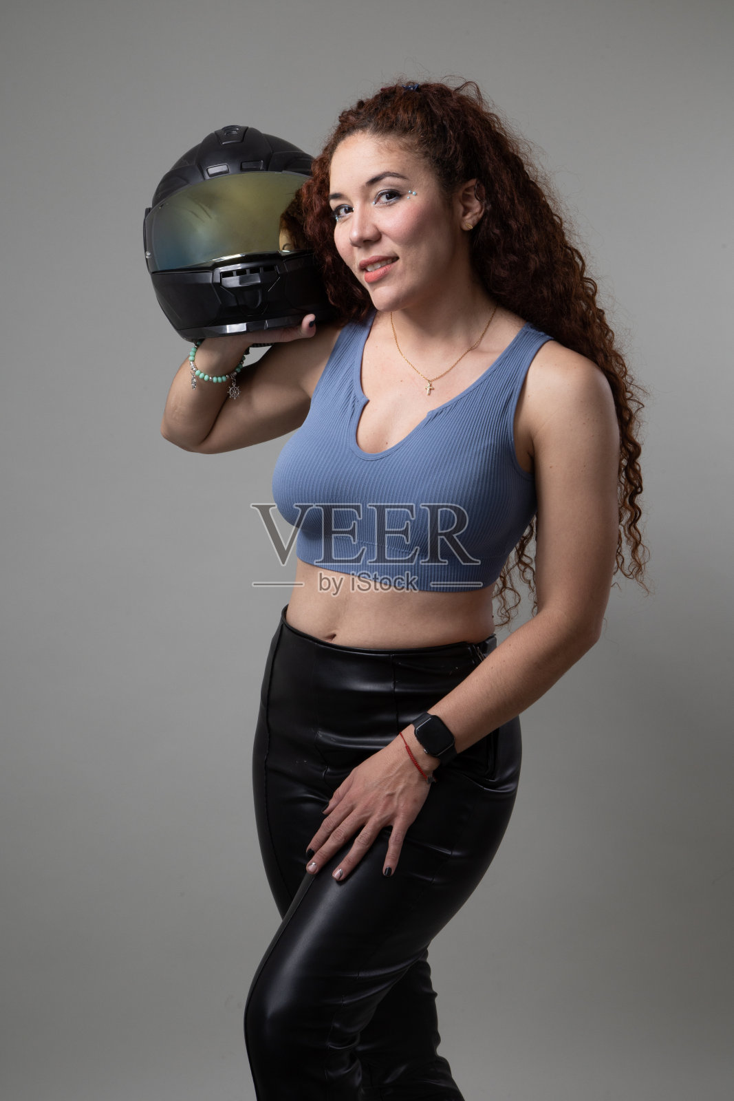 女人拿着摩托车头盔，她有长卷发，安全设备在工作室，生活方式照片摄影图片