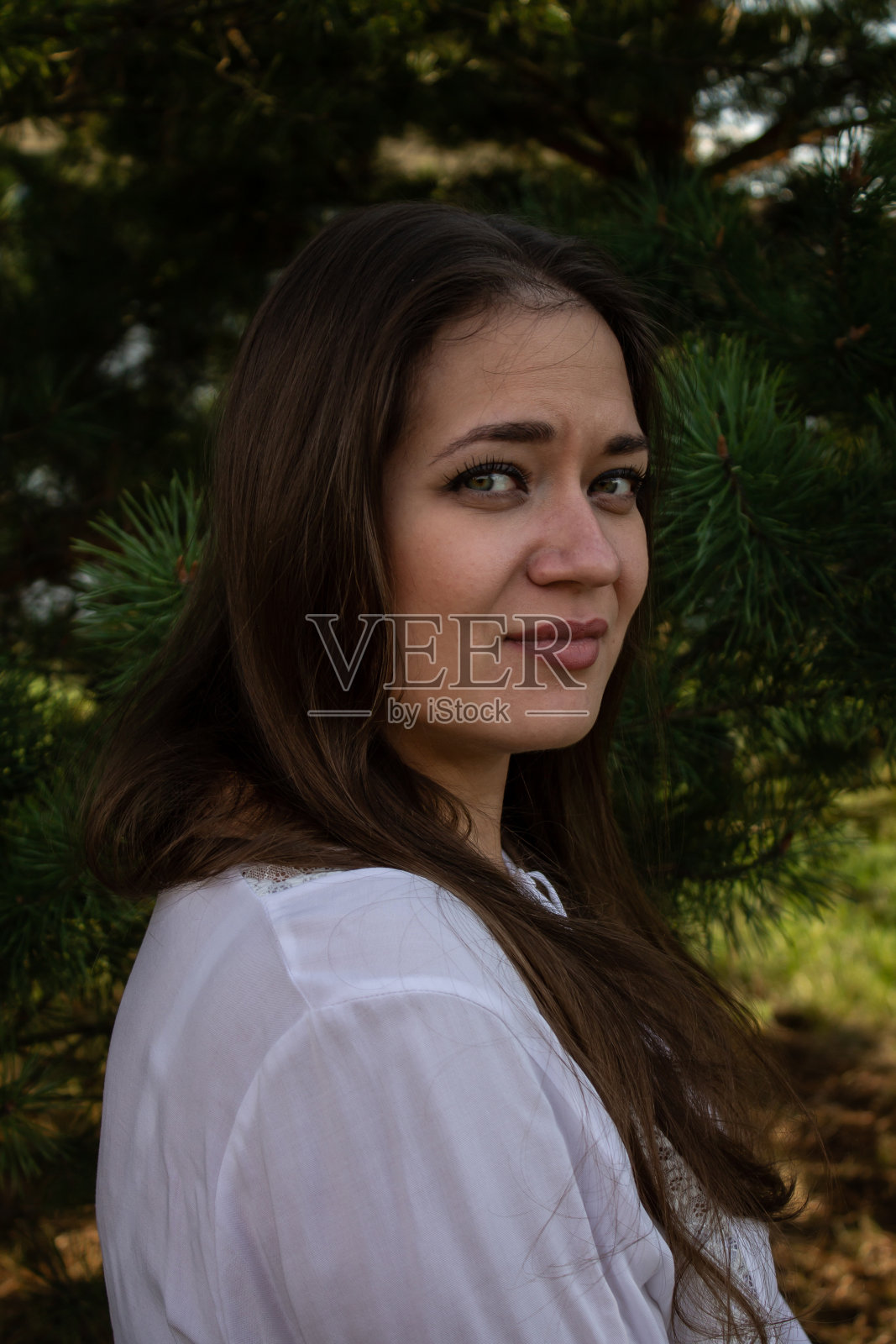 一个年轻的棕色头发的美丽女孩的肖像，绿色的眼睛和一件白色的衬衫在树的背景照片摄影图片