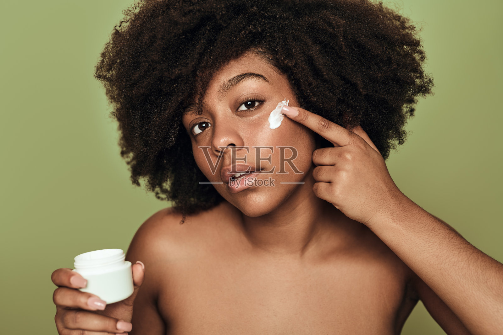 细心的年轻民族妇女在工作室的脸颊上使用保湿霜照片摄影图片