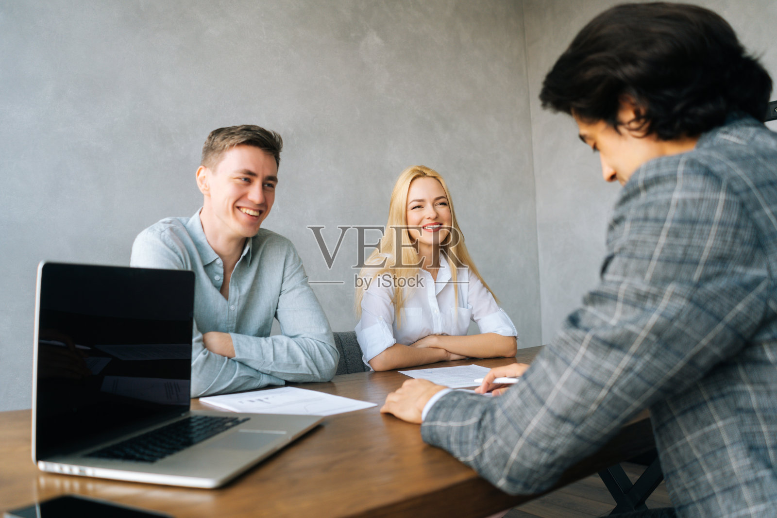 在会议室里，三个兴高采烈的年轻同事坐在桌子前，拿着笔记本电脑和纸质文件，进行业务演示。照片摄影图片