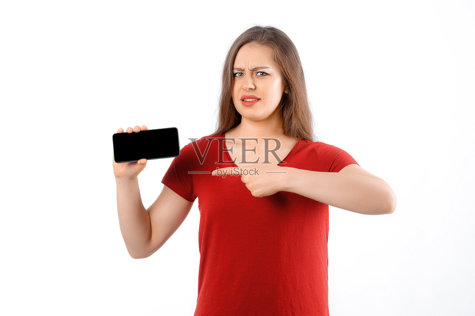 欣喜若狂的女孩拿着智能手机介绍很棒的游戏应用程序展示智能手机食指空白手机屏幕。室内摄影棚拍摄，白色背景照片摄影图片