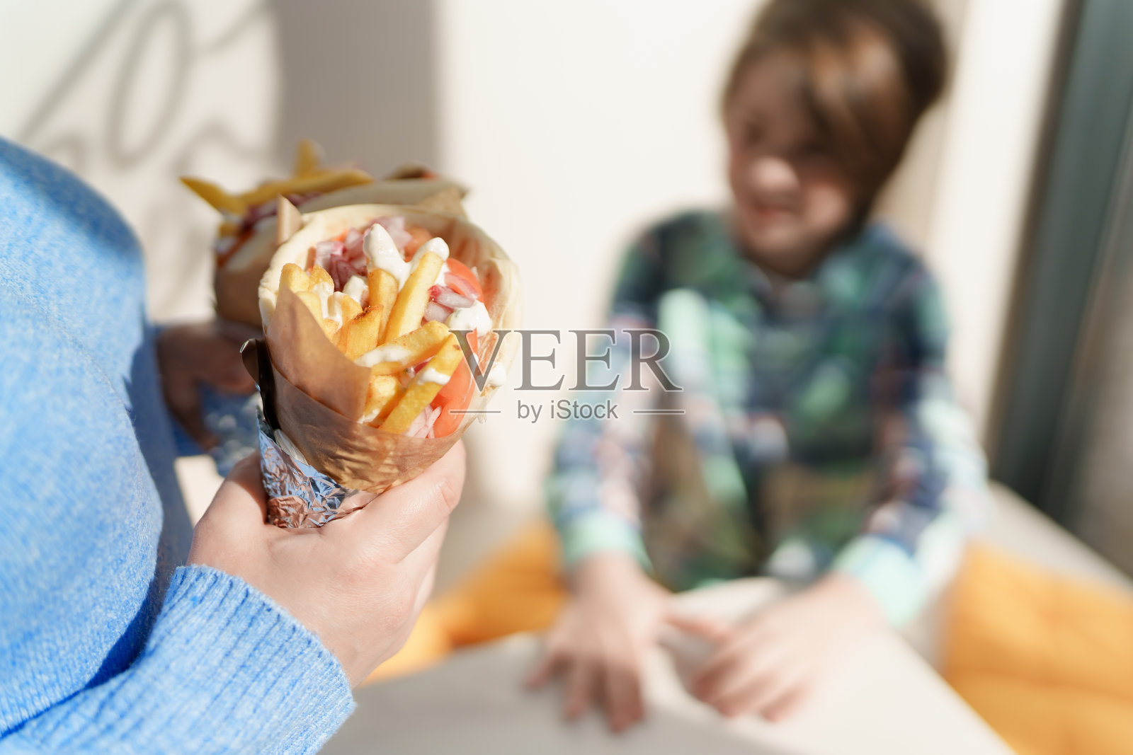 一名妇女把一个陀螺三明治给一个小男孩当午餐。母亲和儿子在咖啡馆享受传统的希腊快餐照片摄影图片