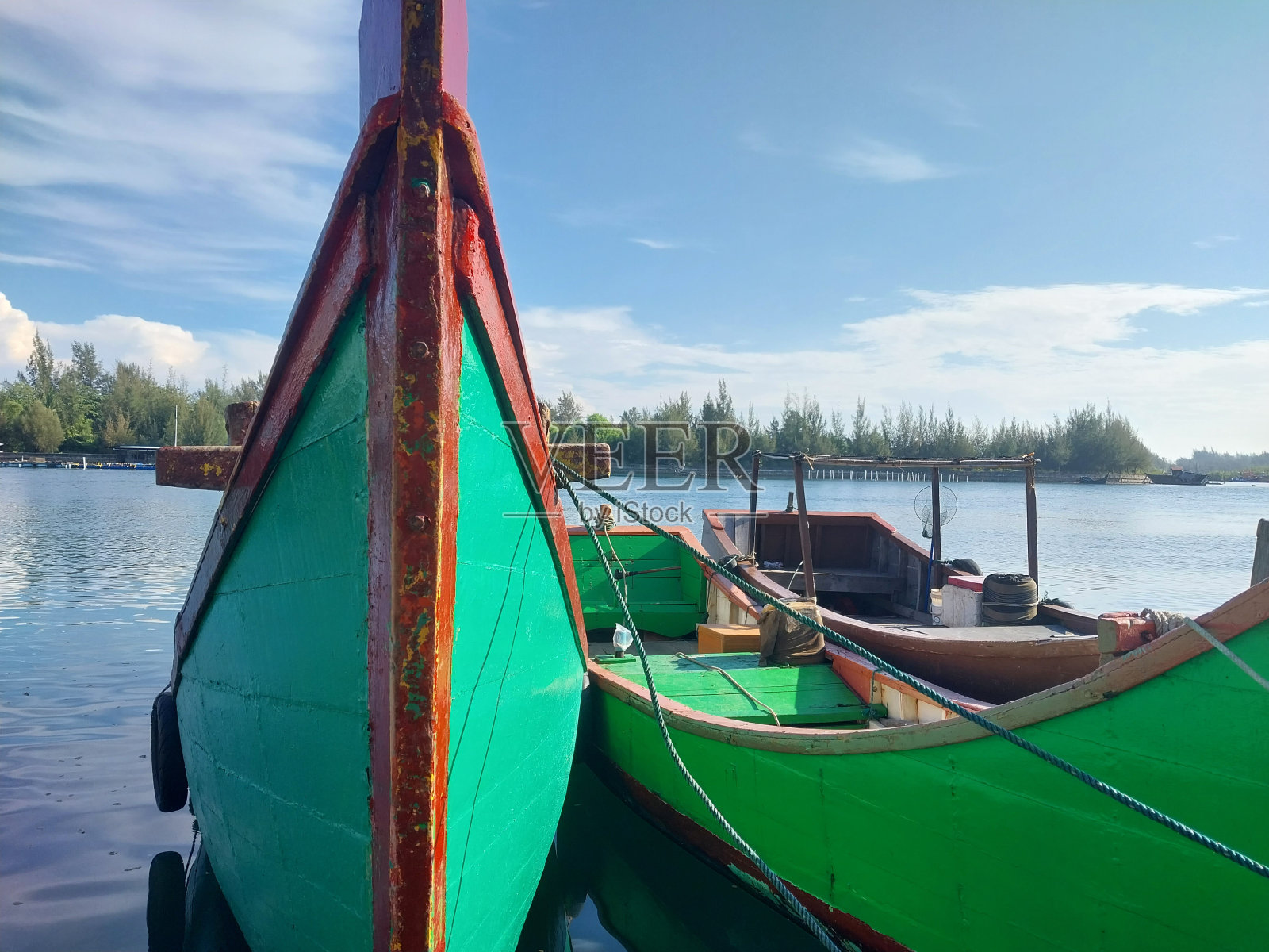 传统渔船停泊在平静的水域:以松林和晴朗的天空为背照片摄影图片